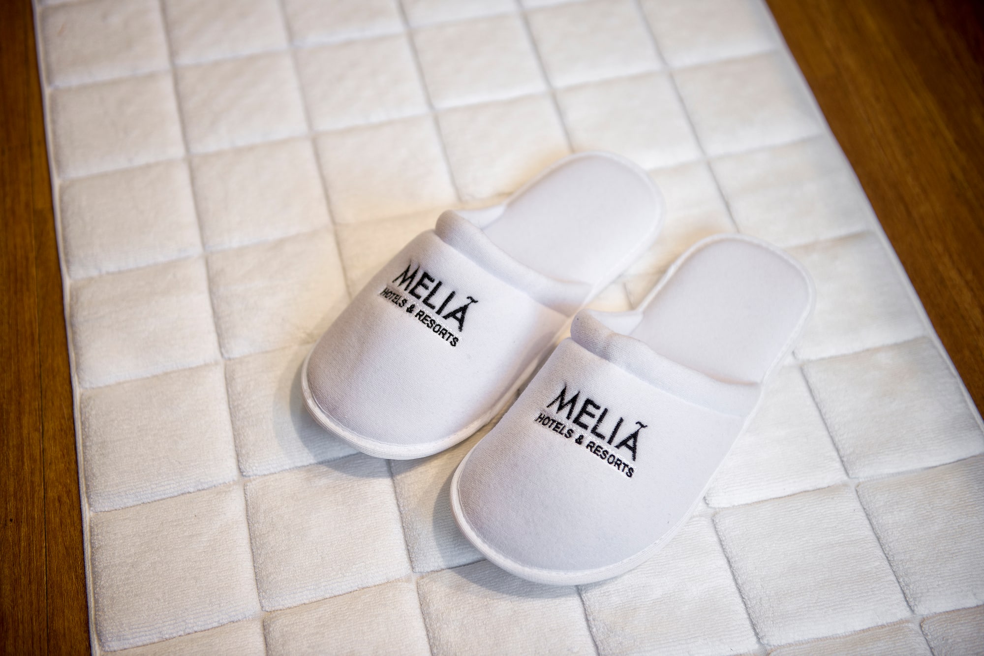 White Meliá Hotels & Resorts guest slippers on hotel bath mat.