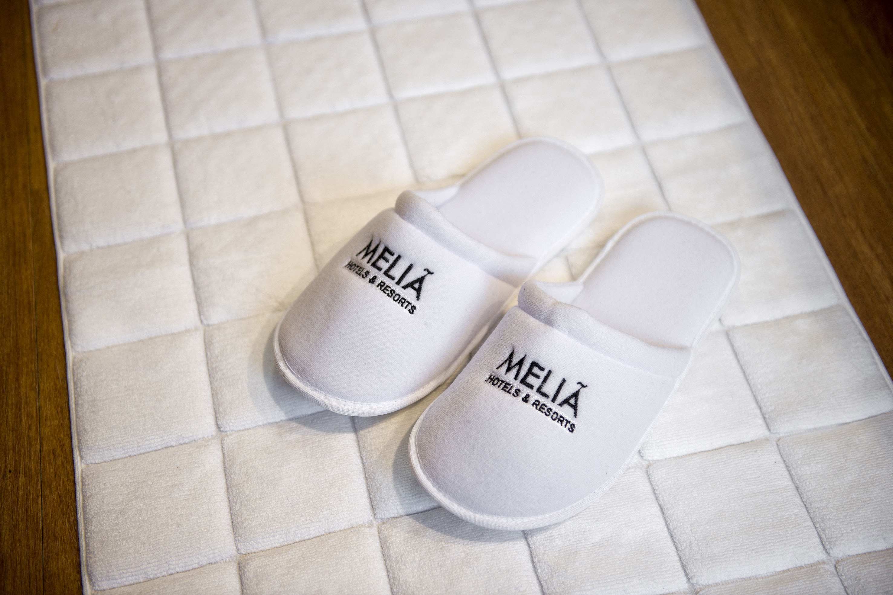 White Meliá Hotels & Resorts guest slippers on hotel bath mat.