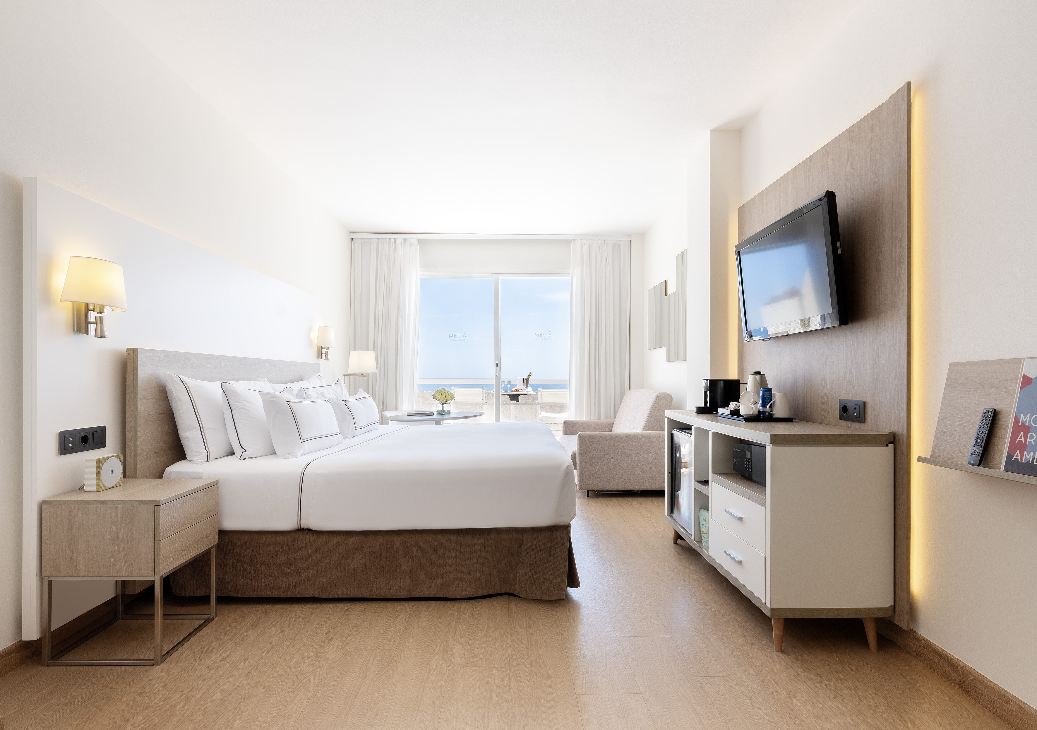 Modern hotel room with sea view, large bed, and private balcony.