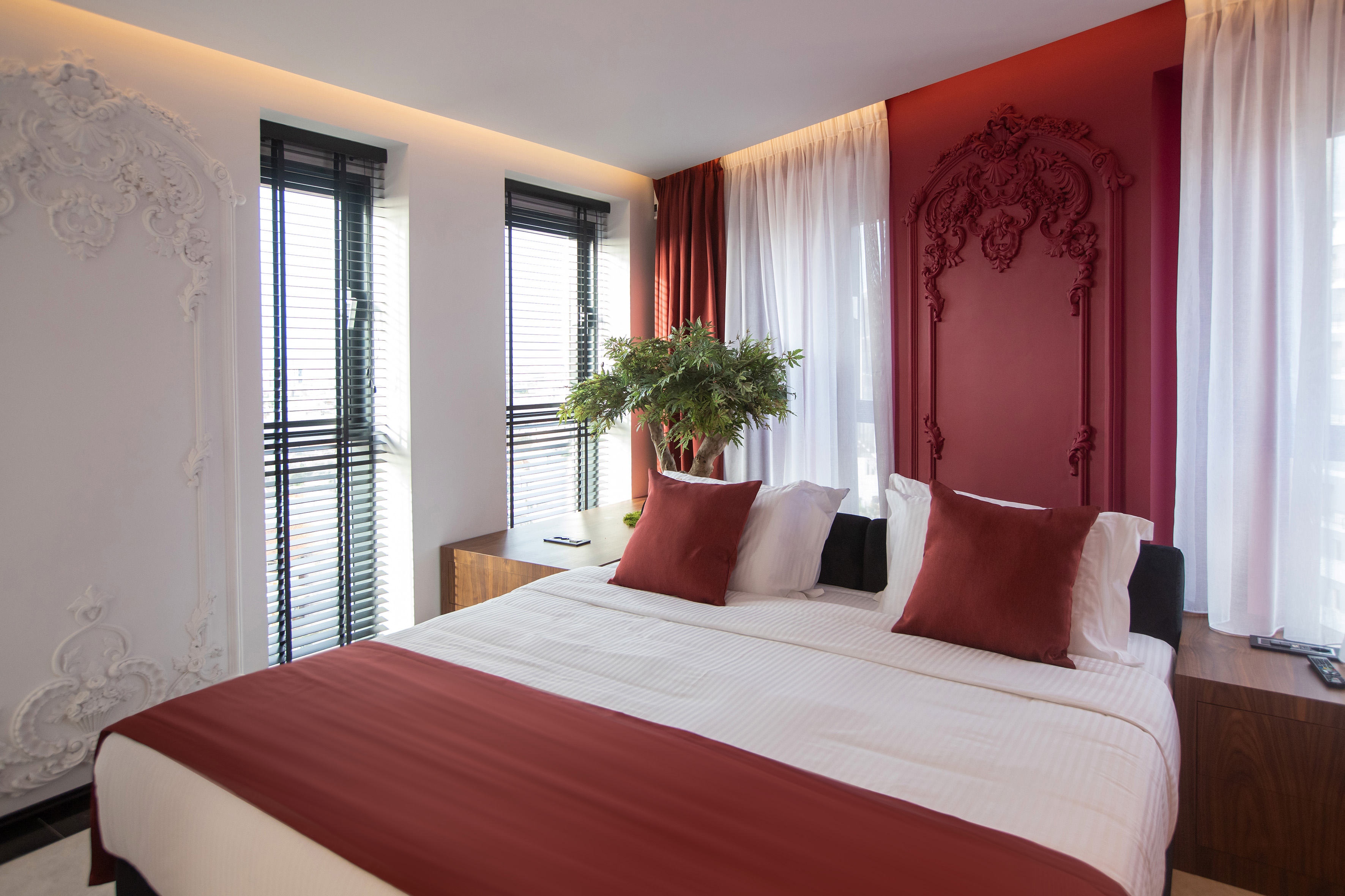 Modern bedroom with red ornate wall paneling, white bed, and window blinds.