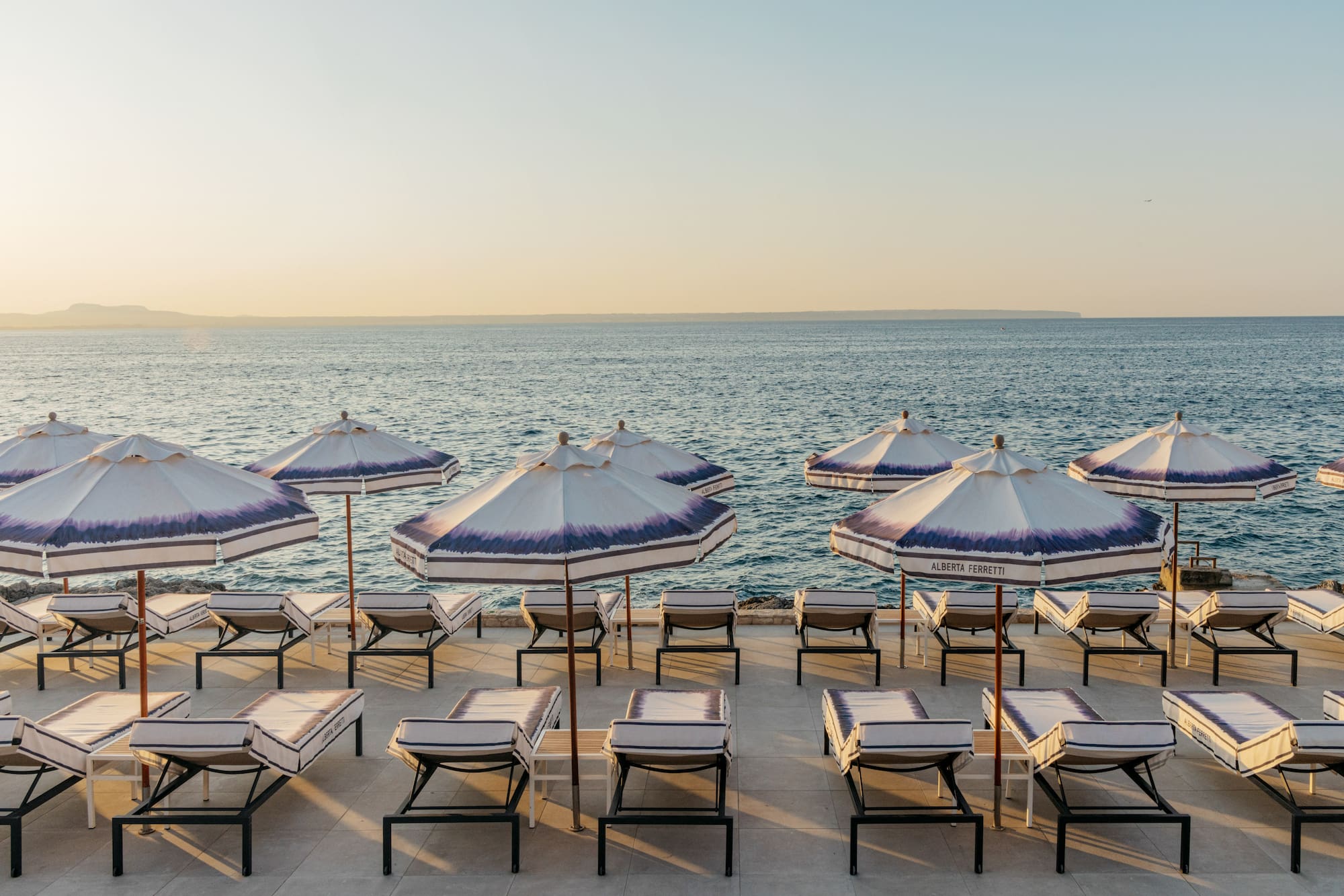 Alberta Ferretti striped beach umbrellas and lounge chairs by the ocean.