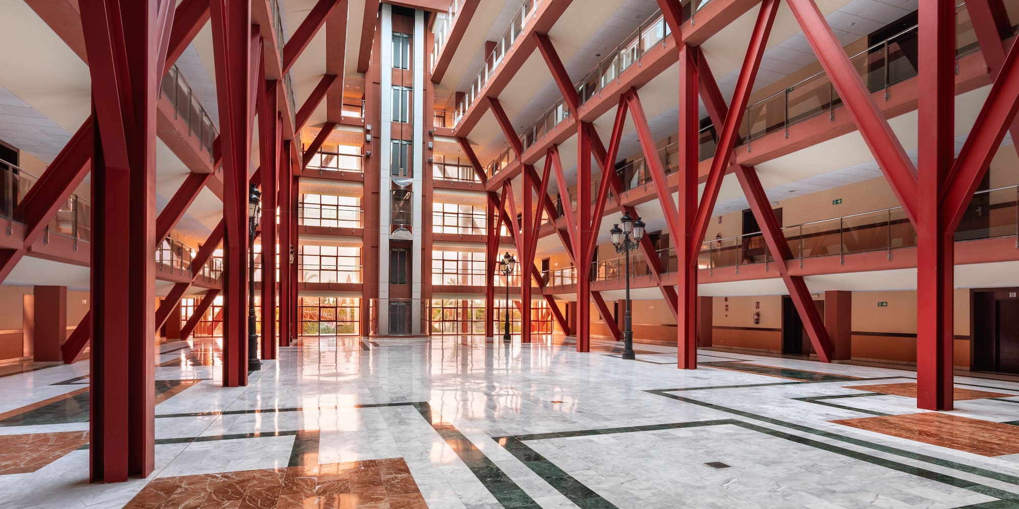 Modern atrium, red beams, glass elevator, patterned marble floor.