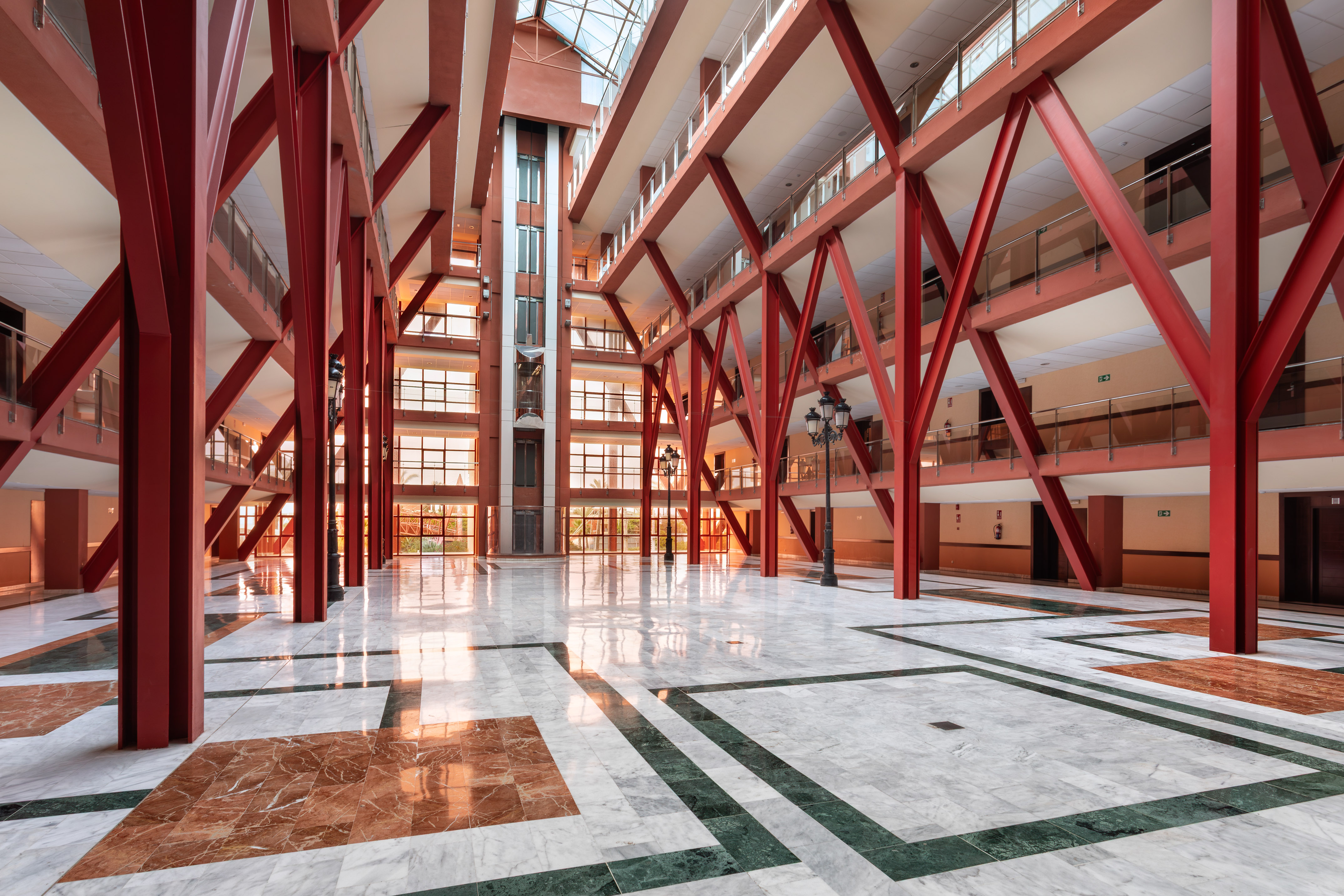 Modern atrium, red beams, glass elevator, patterned marble floor.