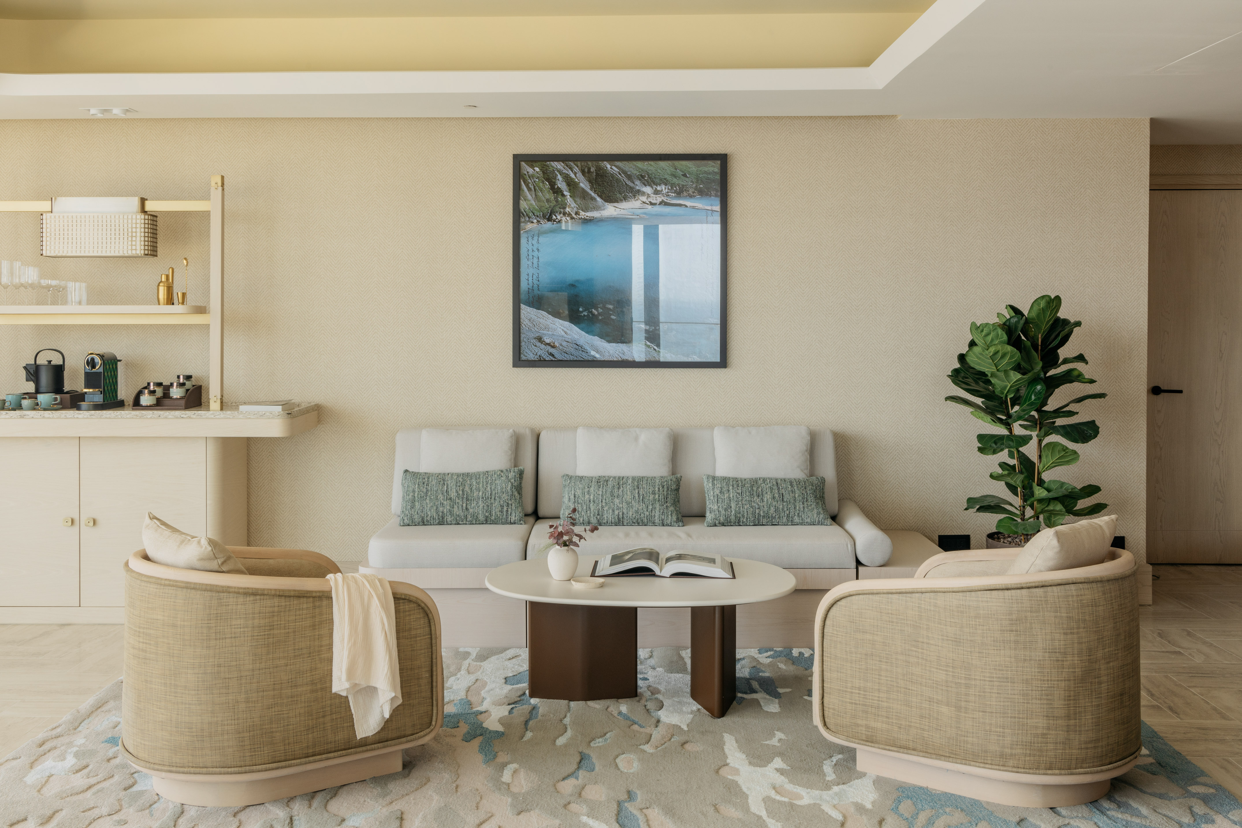 Modern hotel lounge with beige sofa, armchairs, framed artwork, and coffee bar.