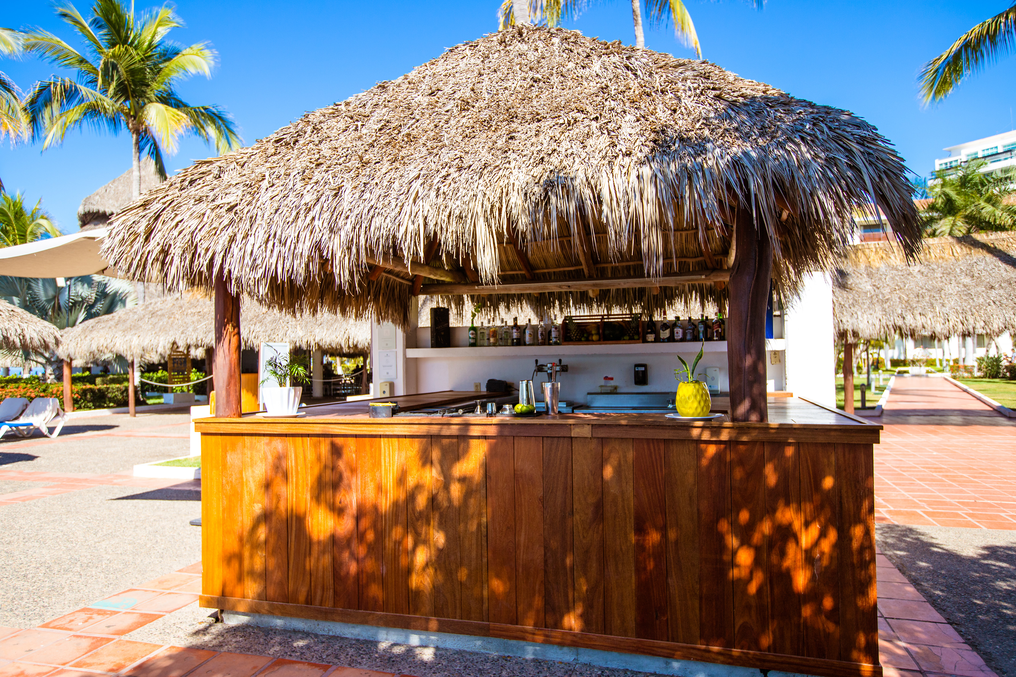 Sunny outdoor tiki bar with thatched roof and wooden counter.