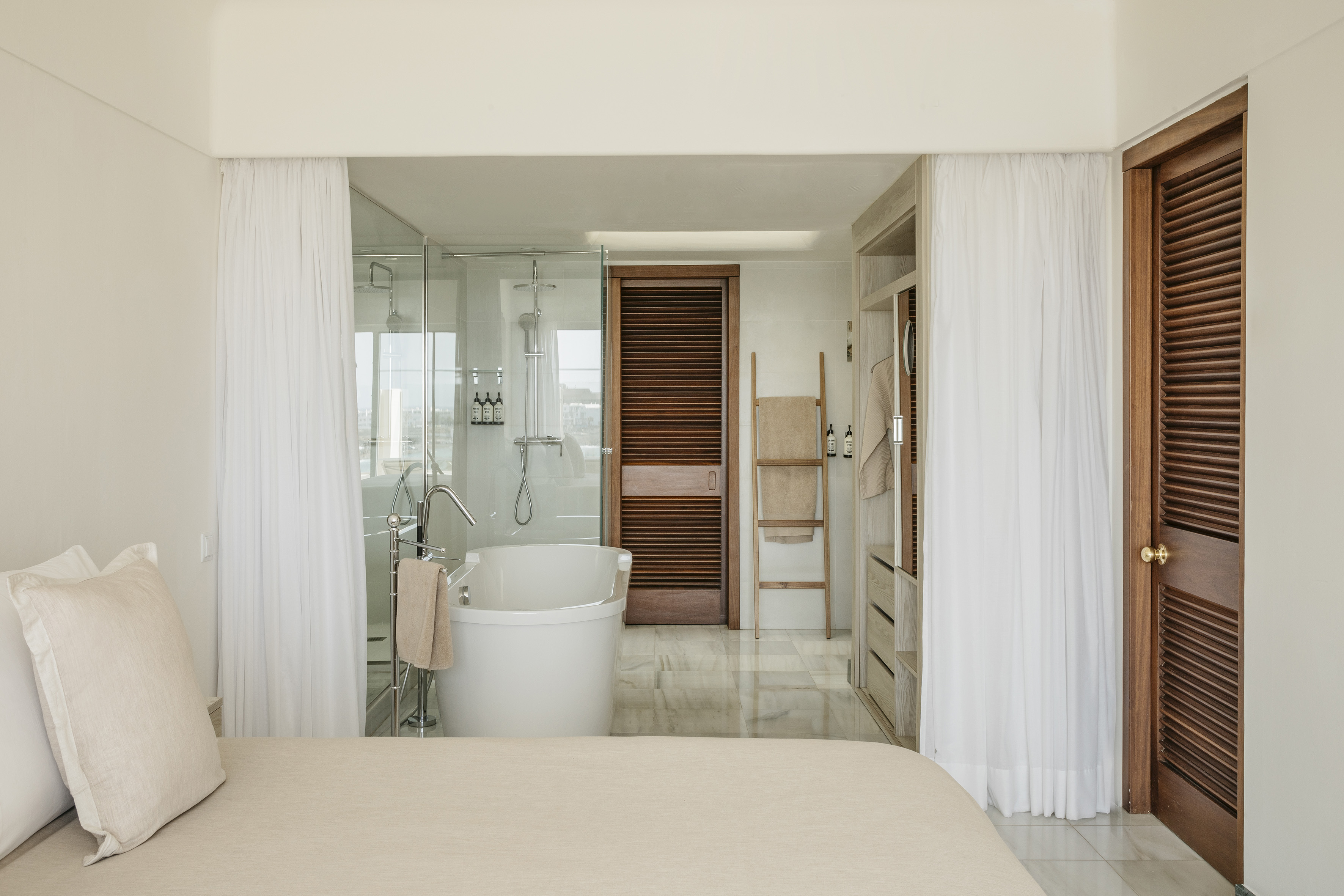 Modern hotel room: open bathroom with freestanding tub and glass shower.