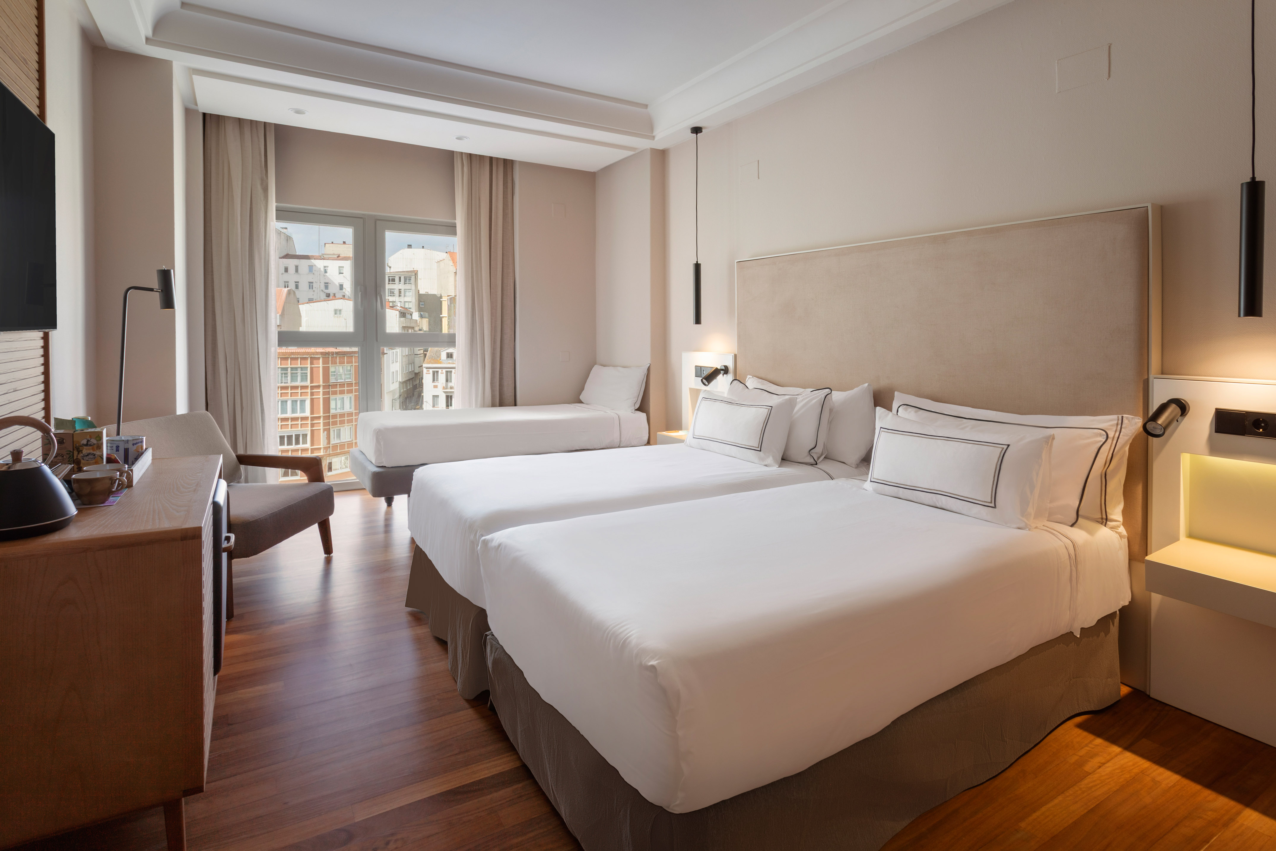 Modern hotel room with twin beds, extra bed, and city view.