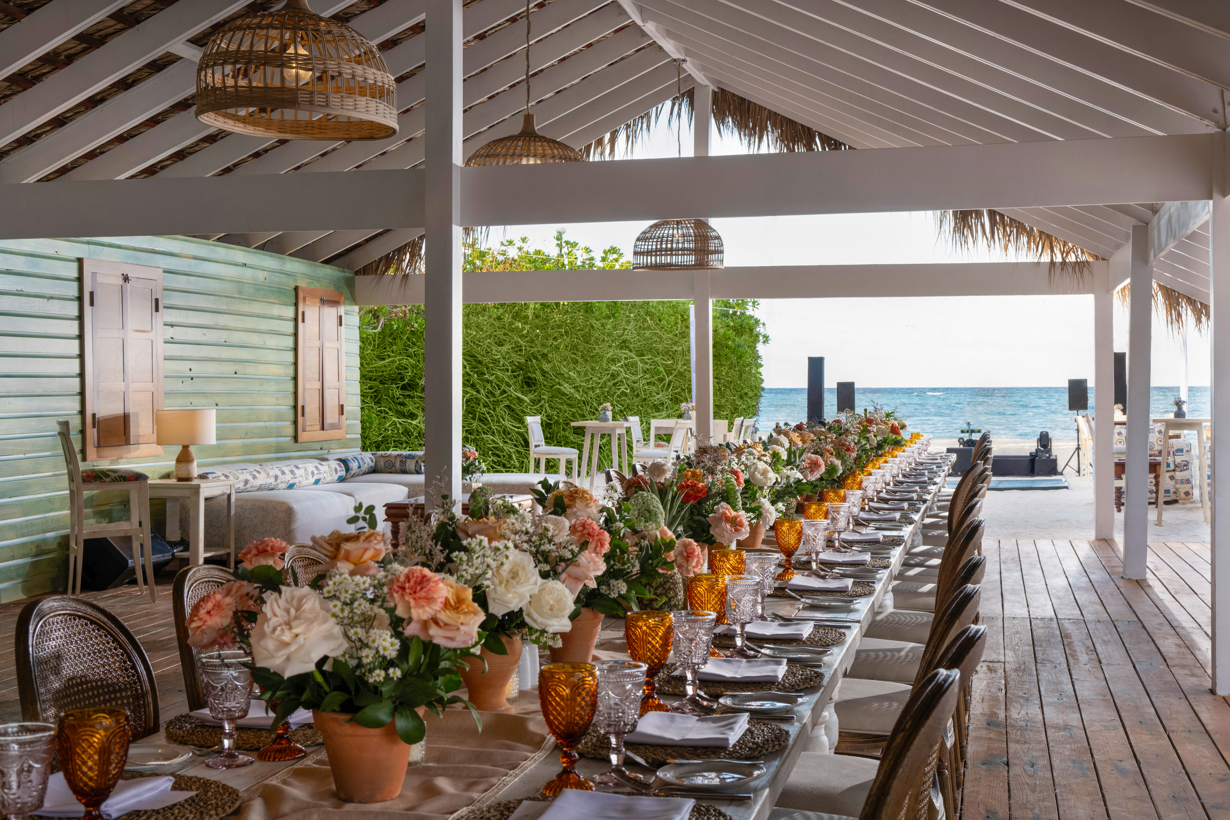 Beachfront dining table, vibrant floral decor, amber glasses, ocean view.