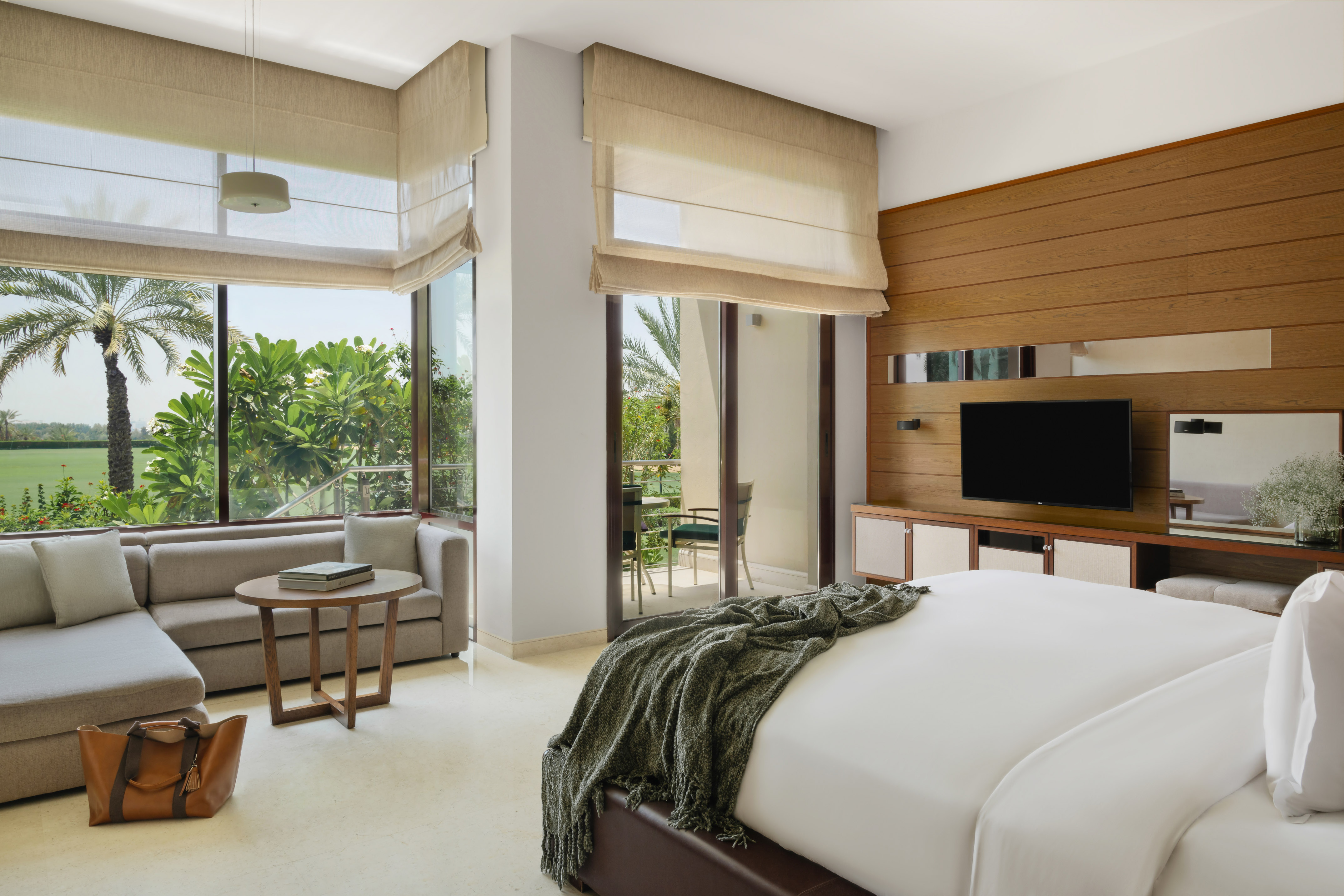Modern hotel bedroom with garden view, private balcony, bed, and lounge area.