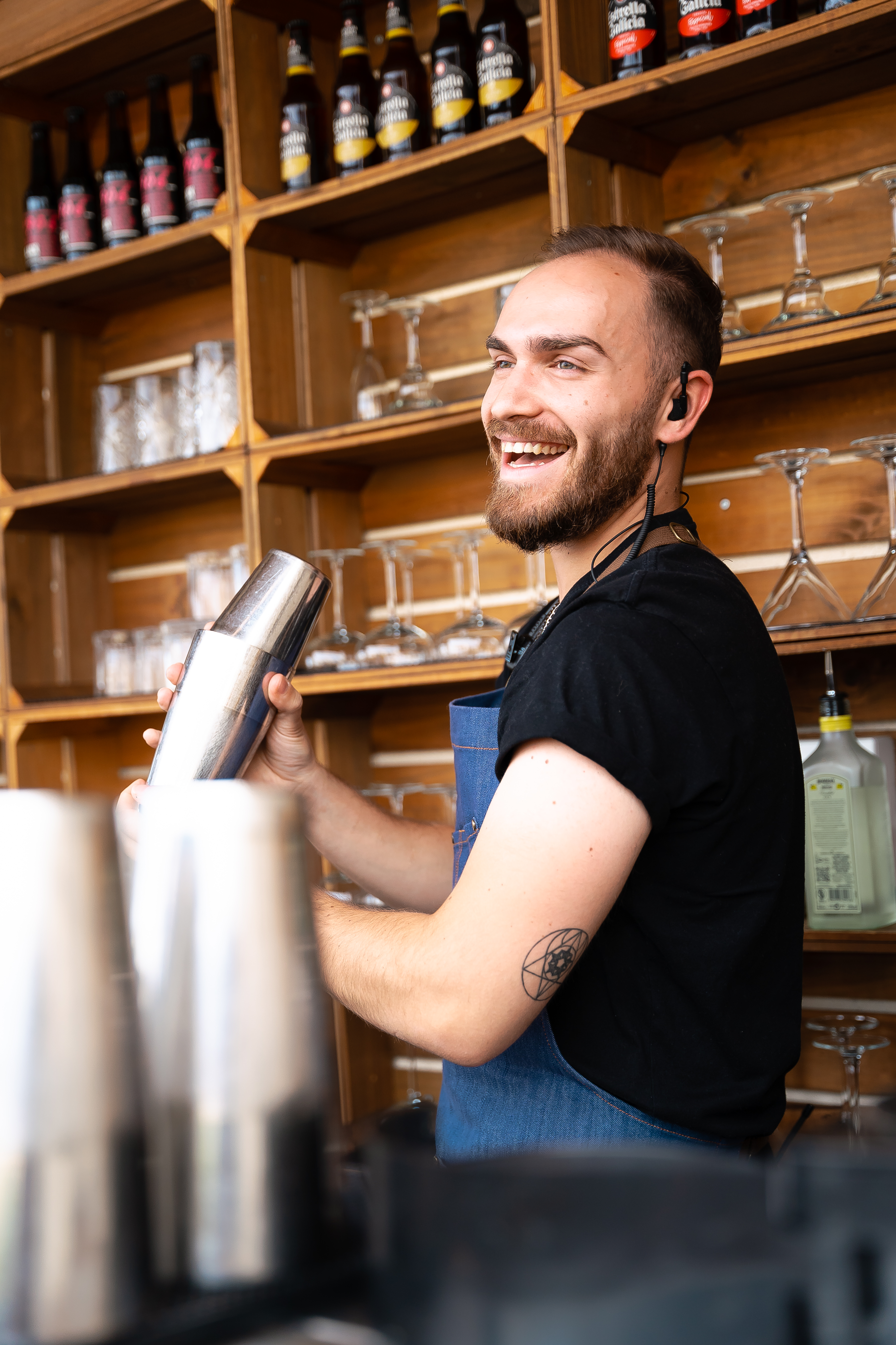 a man wearing a black shirt and blue apron holding a shaker