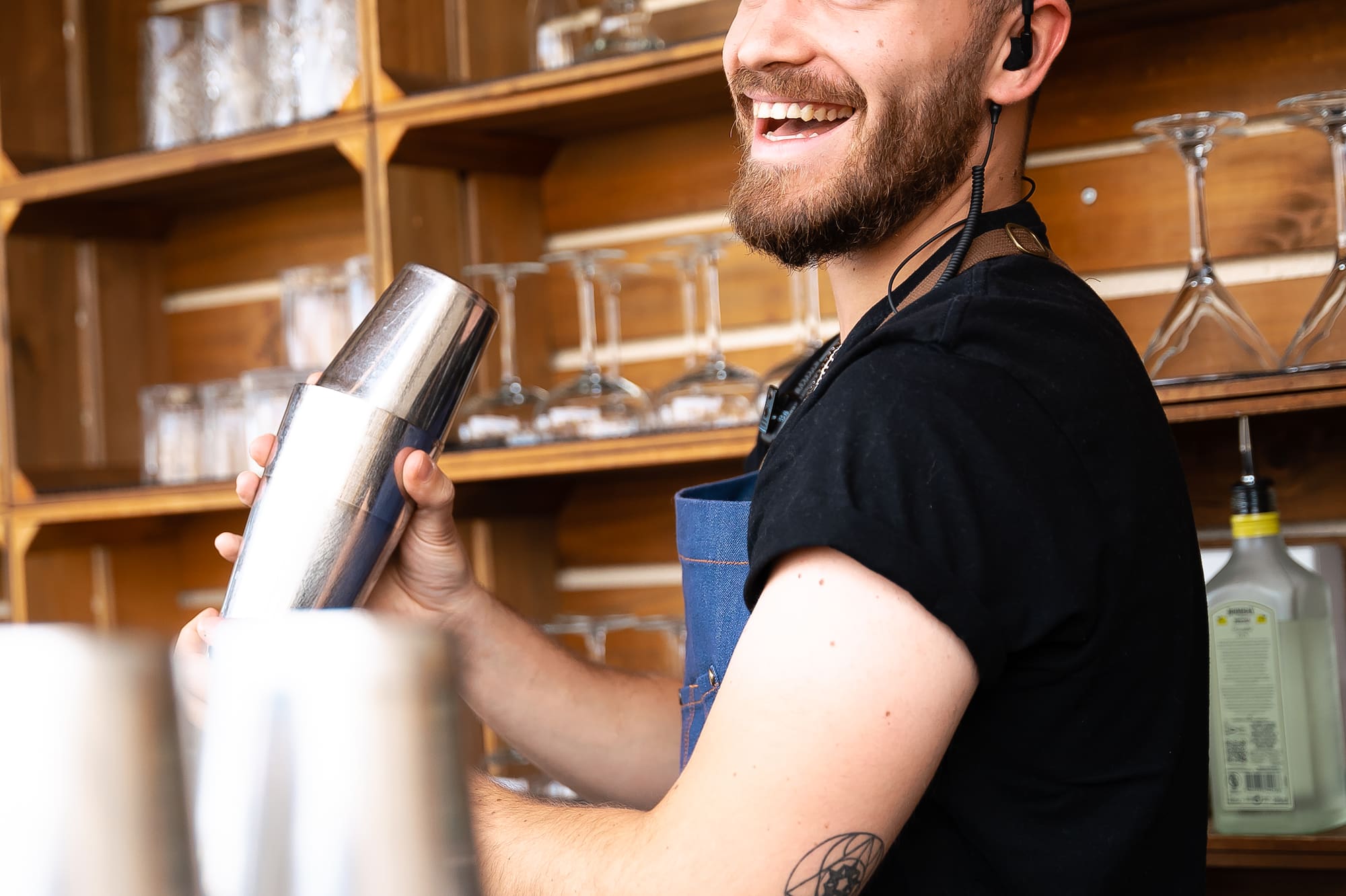 a man wearing a black shirt and blue apron holding a shaker