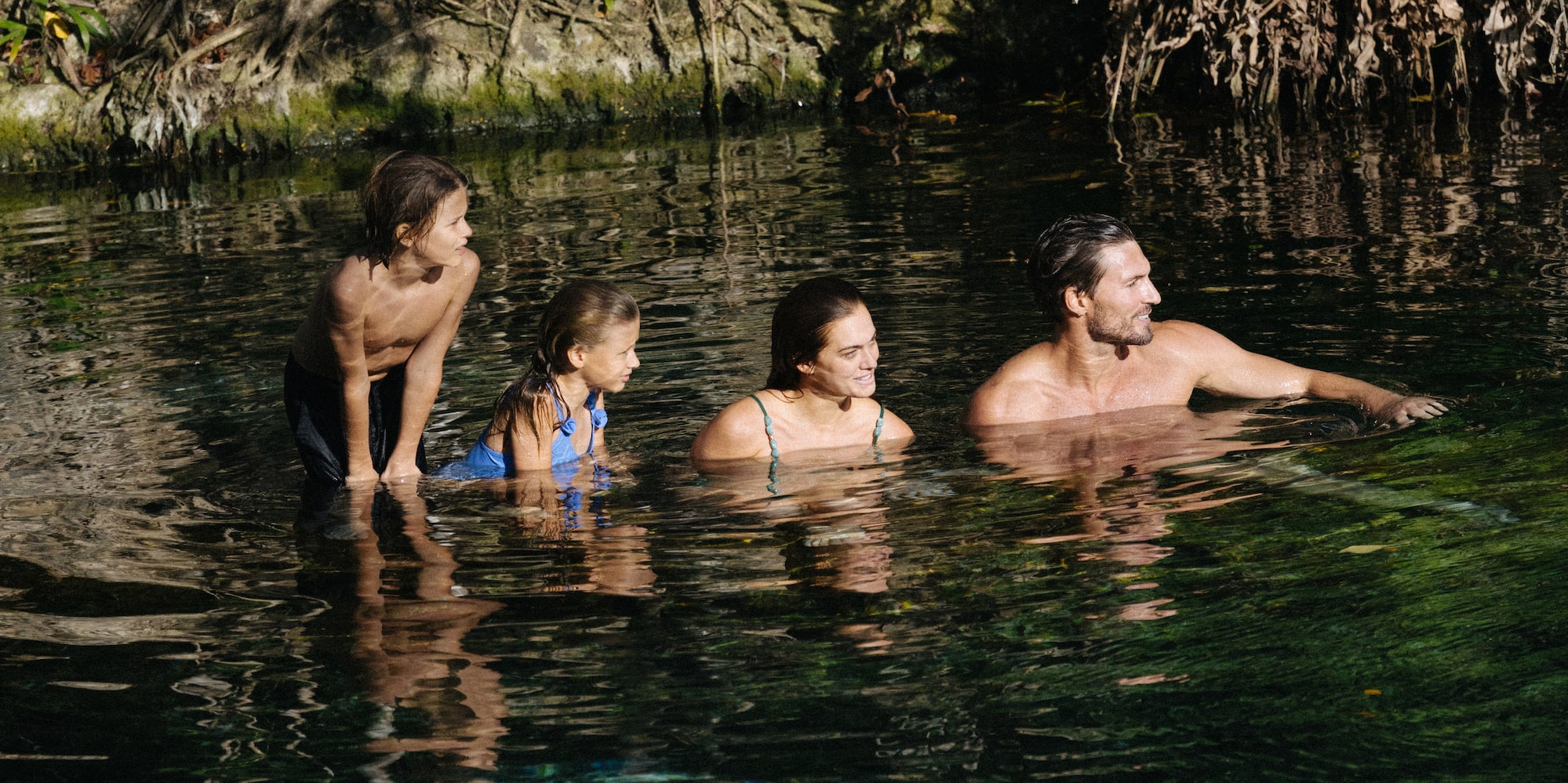 Family of four swimming in a clear jungle cenote.