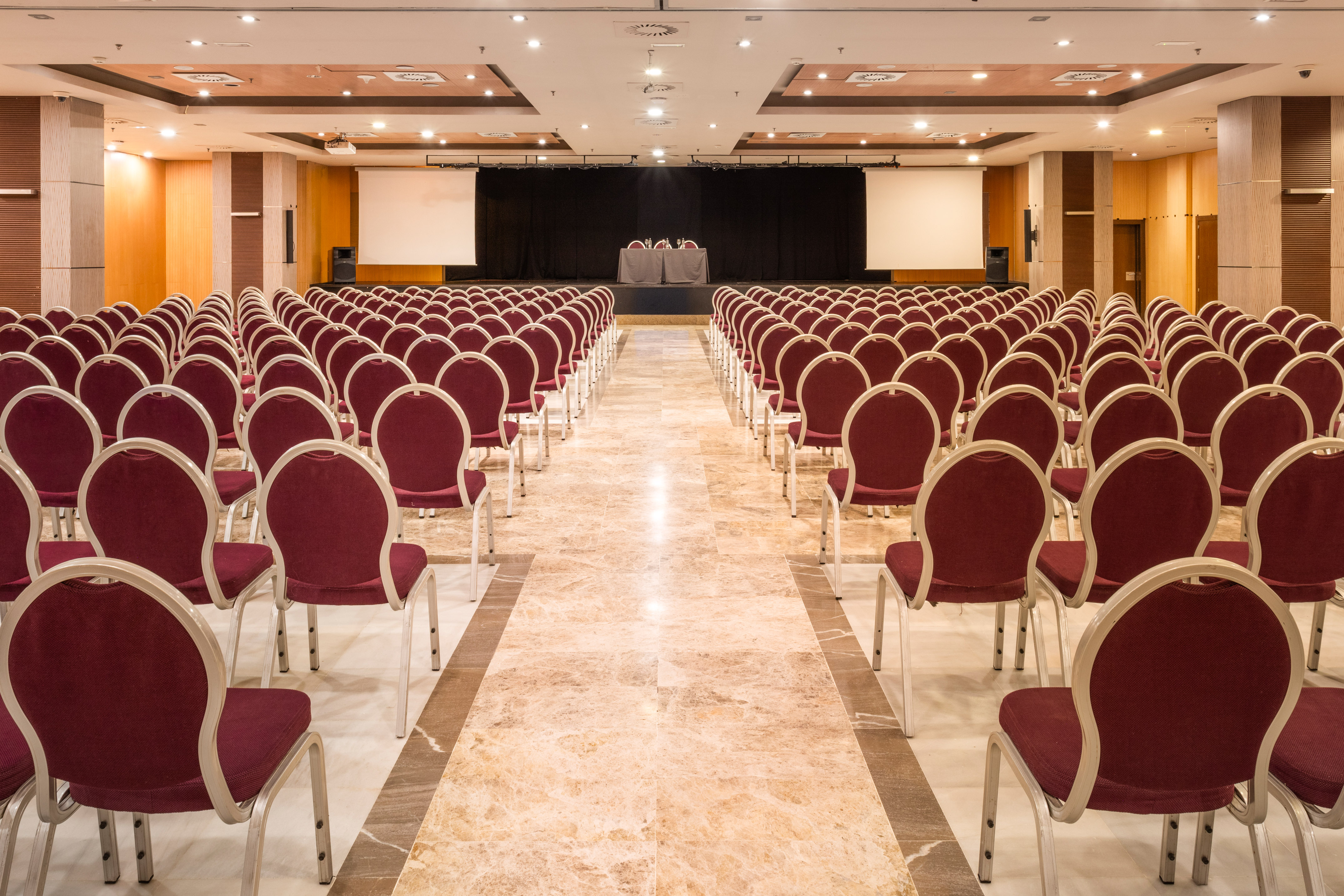 Empty conference room with red chairs, stage, and dual projector screens.