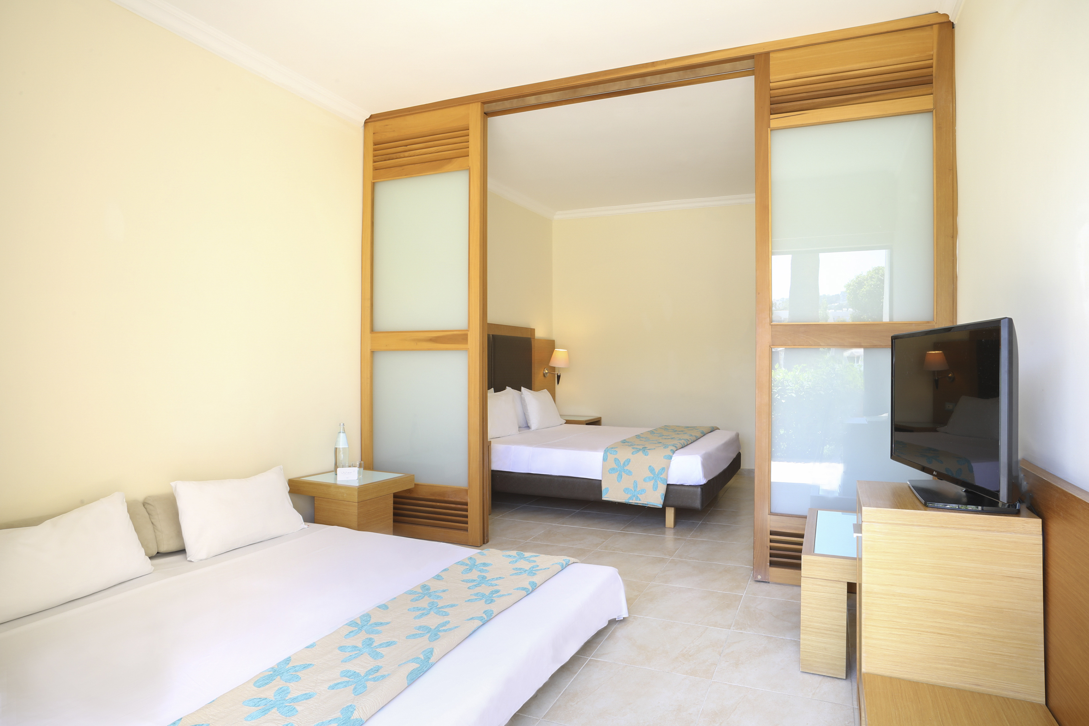 Connected hotel bedrooms with two beds, white linens, and modern sliding doors.