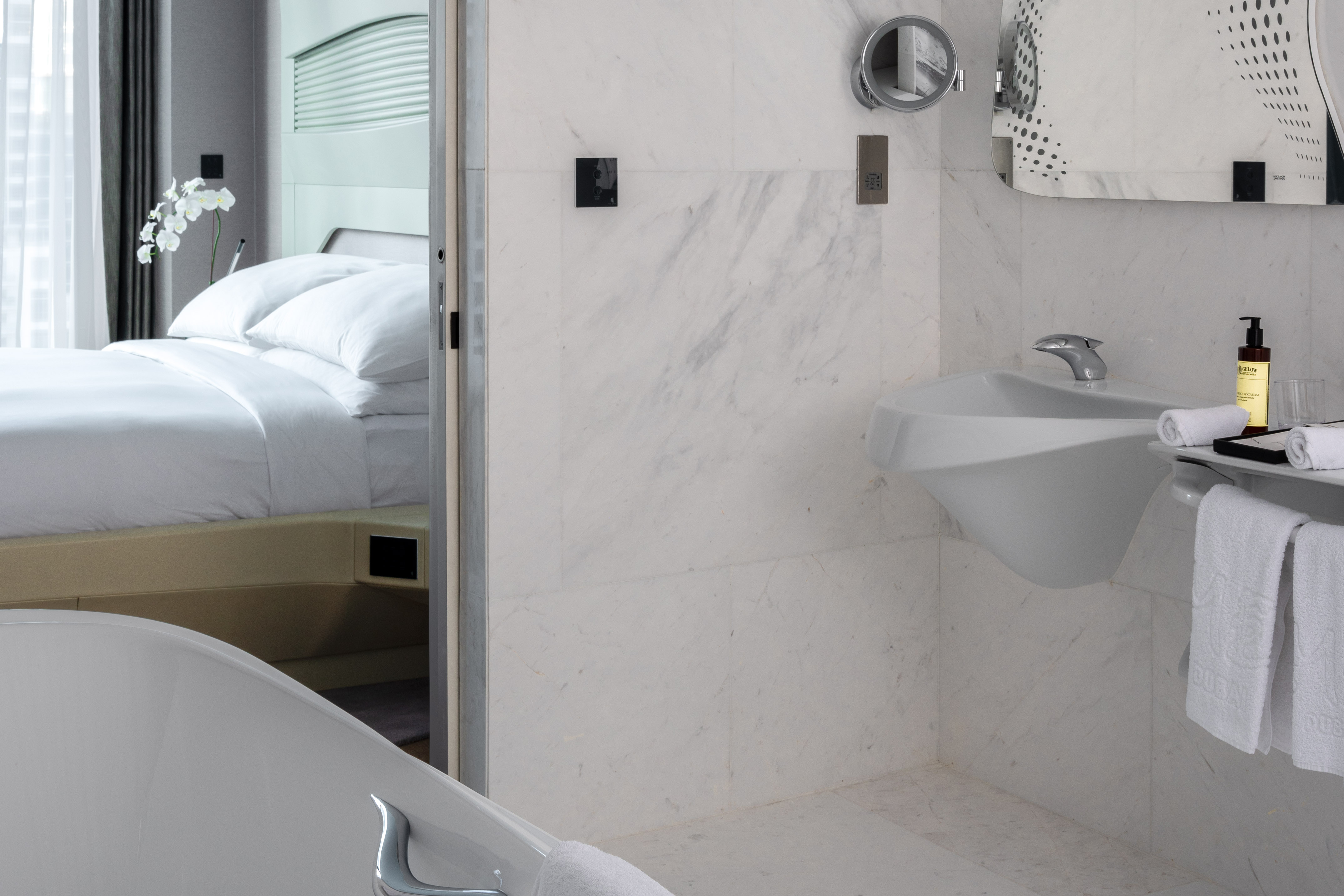 Modern hotel bathroom with white marble, sleek sink, and bedroom view.