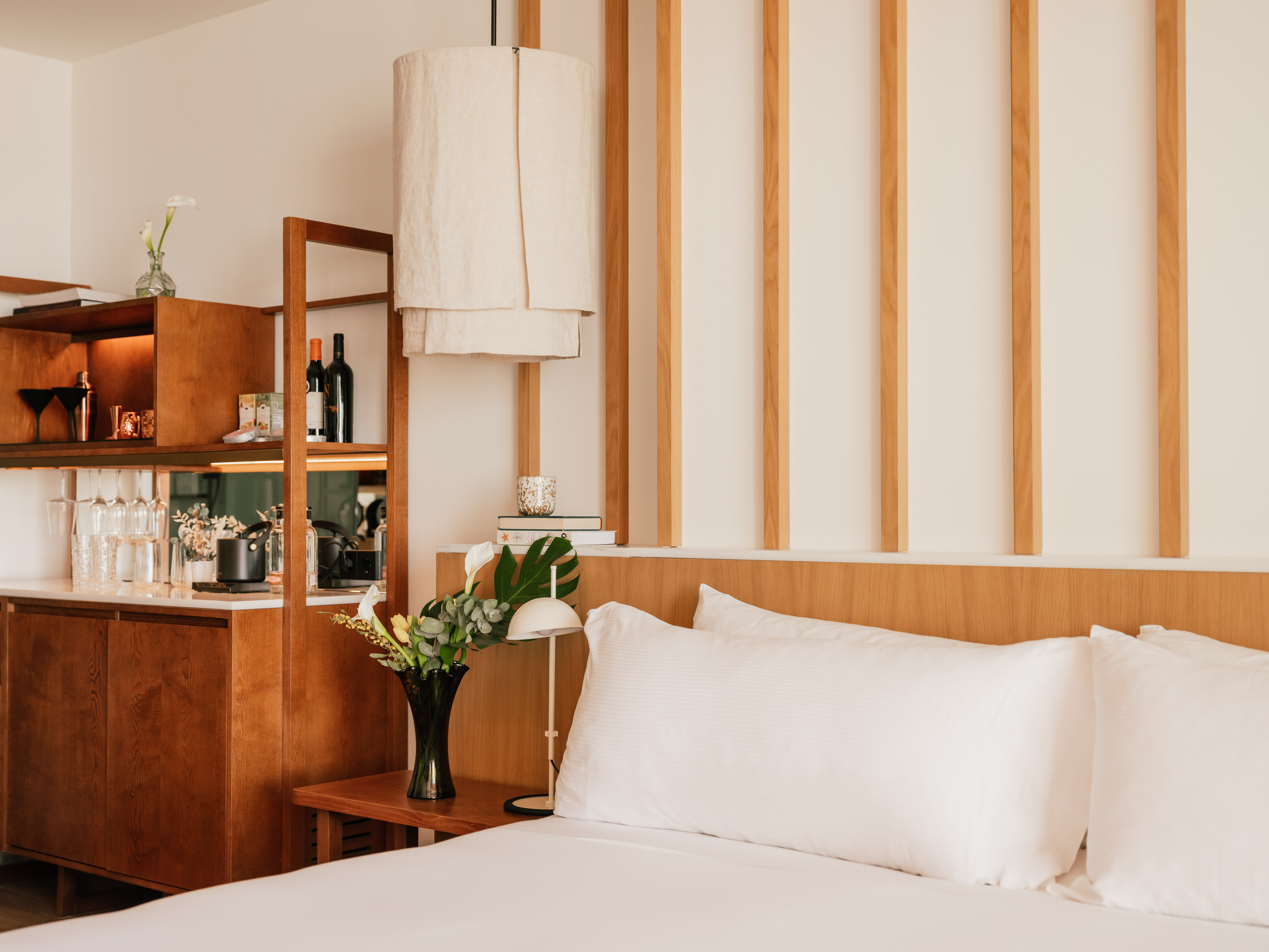 Modern hotel room with white bed, wood accents, and built-in minibar.