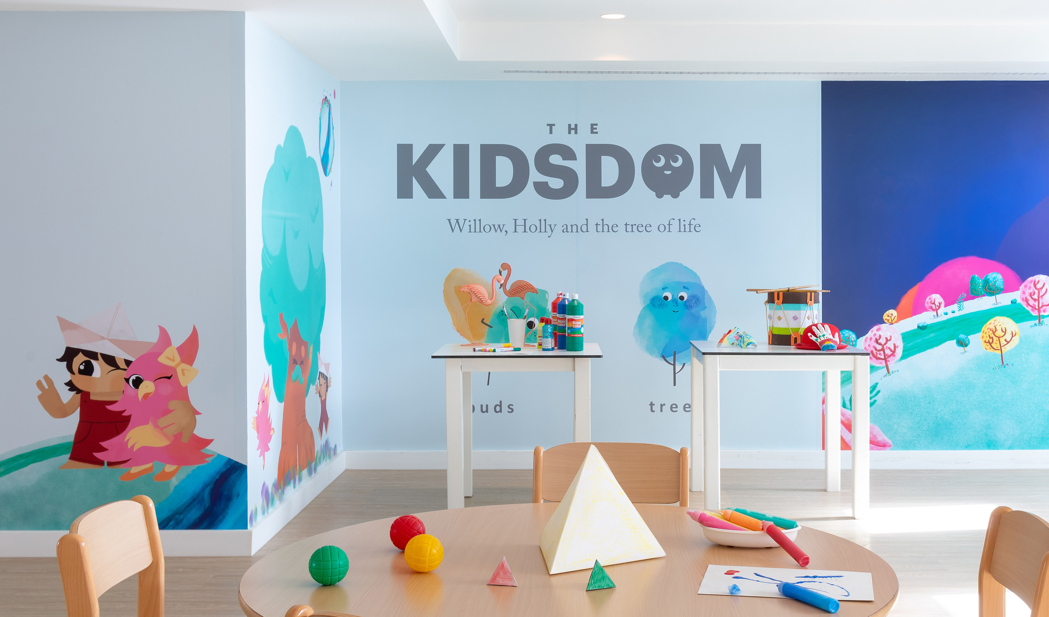 Kids' colorful art room with 'The Kidsdom' mural, craft tables, and art supplies.