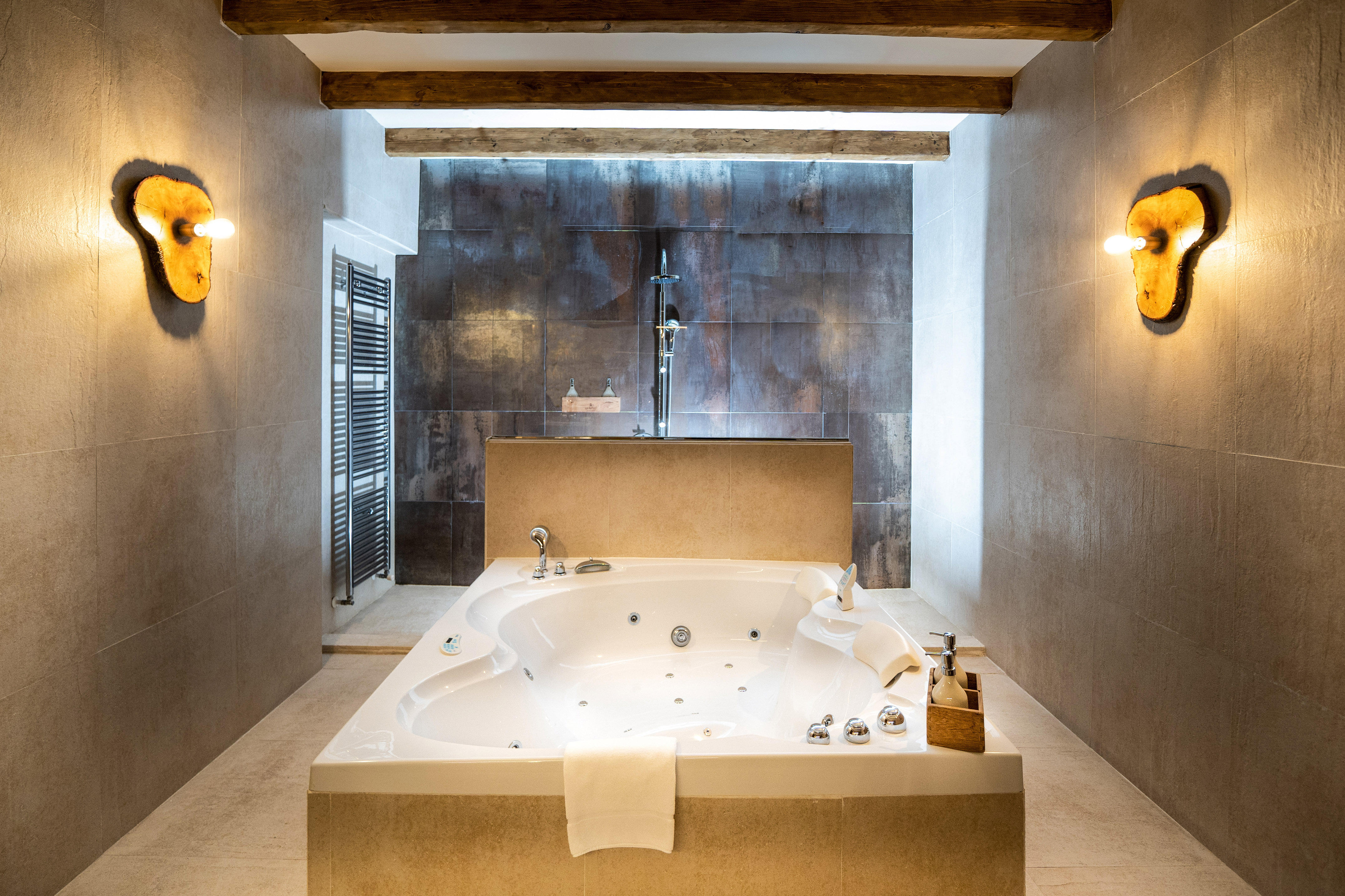 Luxury bathroom with white jacuzzi, shower, modern tiles, and wooden beams.