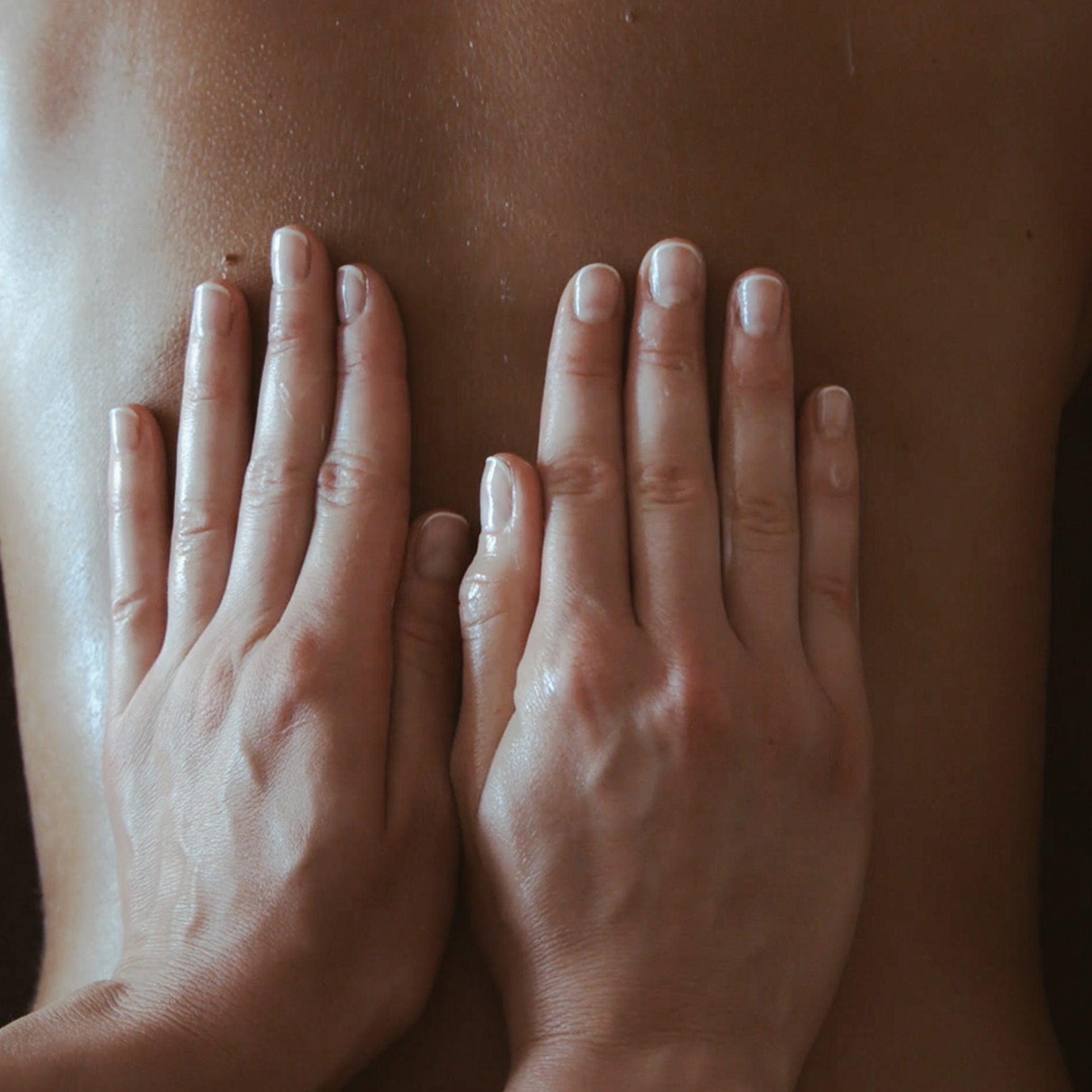Hands performing a relaxing back massage with oil on skin.