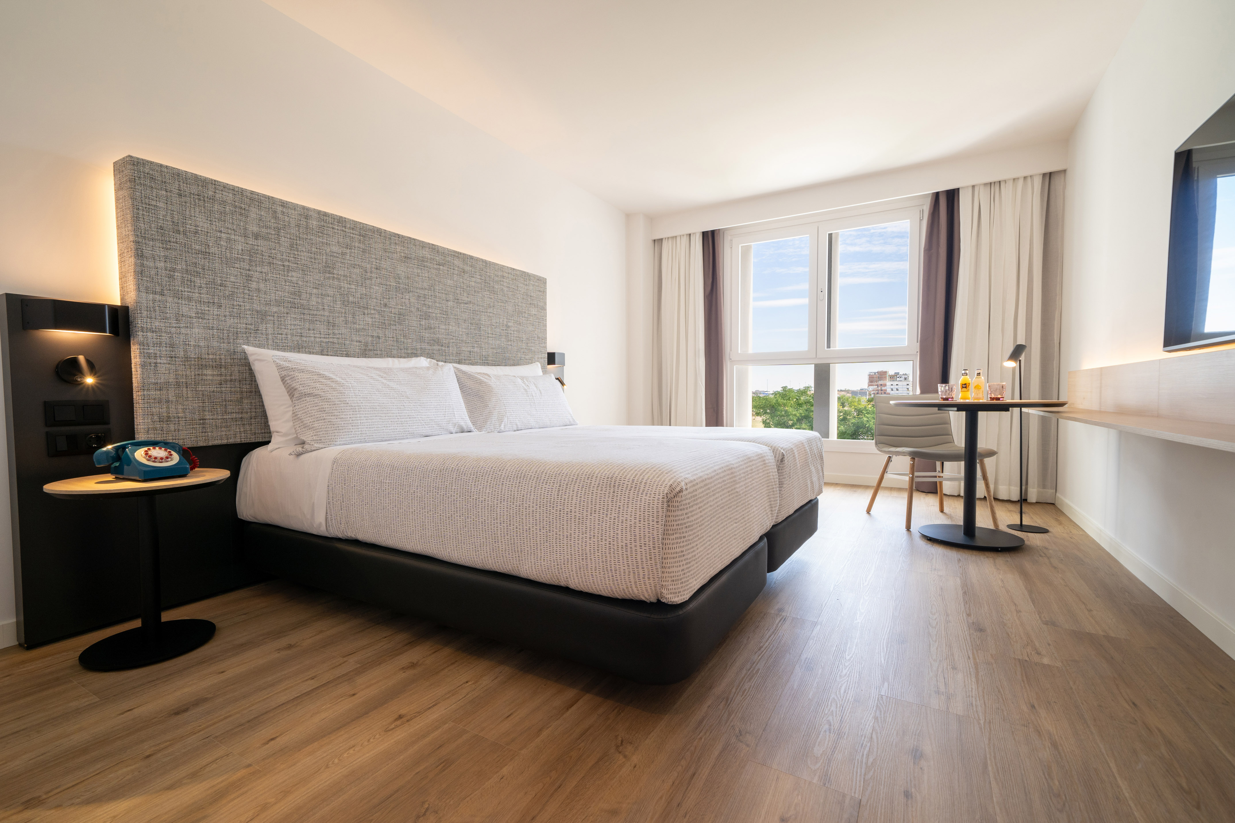 Bright hotel bedroom with twin beds, modern decor, and cityscape view.