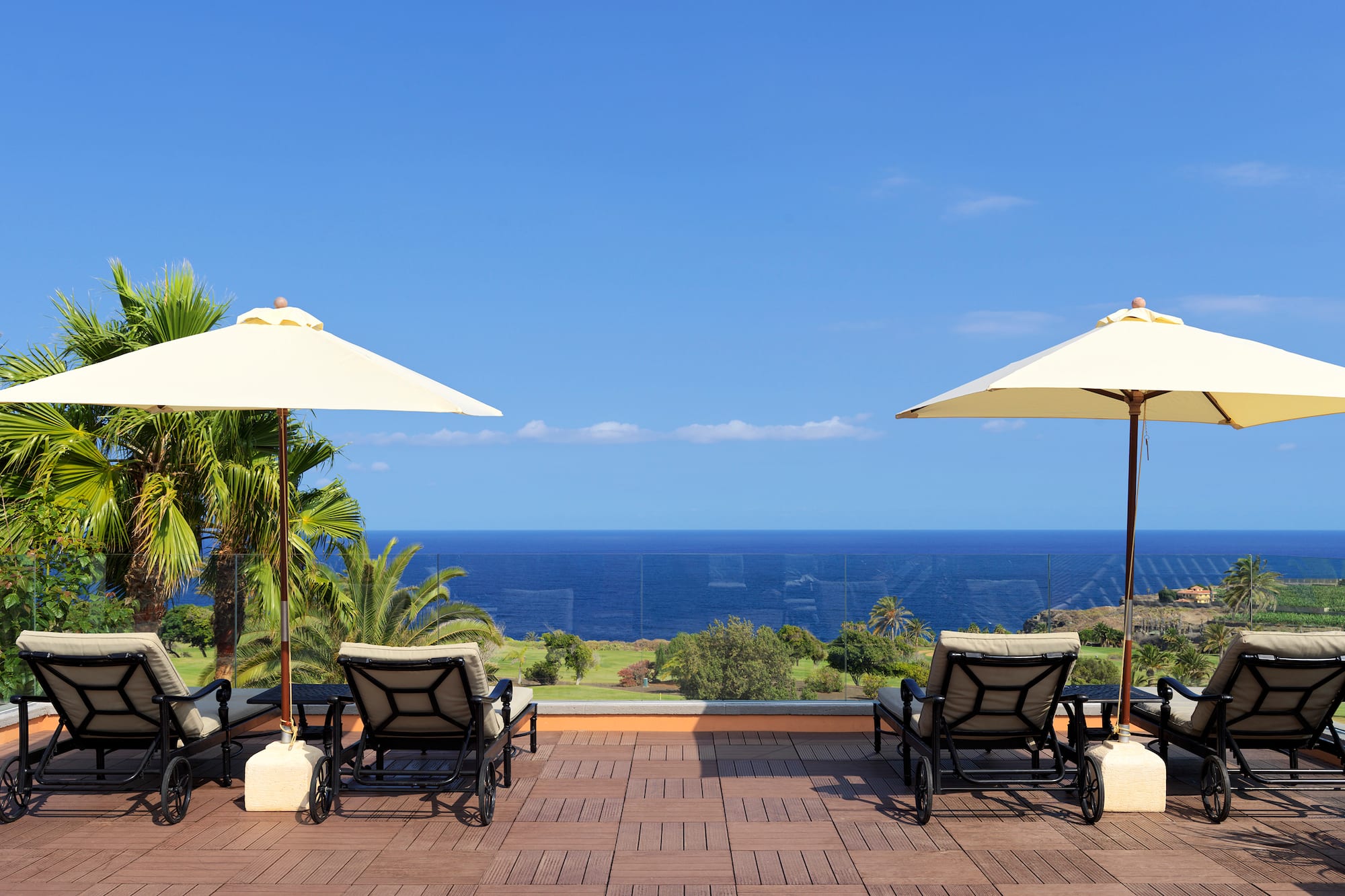 Lounge chairs and parasols on an oceanfront deck with tropical sea view.
