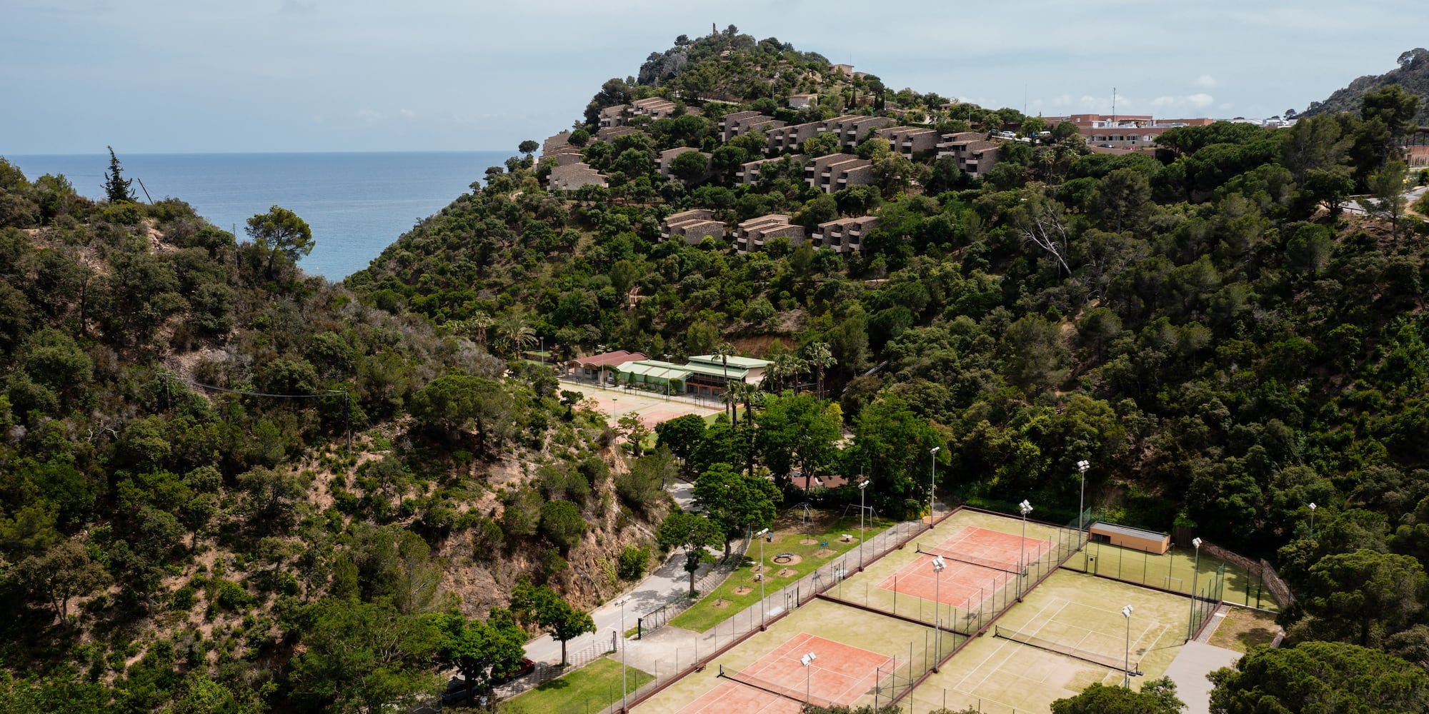 a tennis court and a large hill with trees and buildings