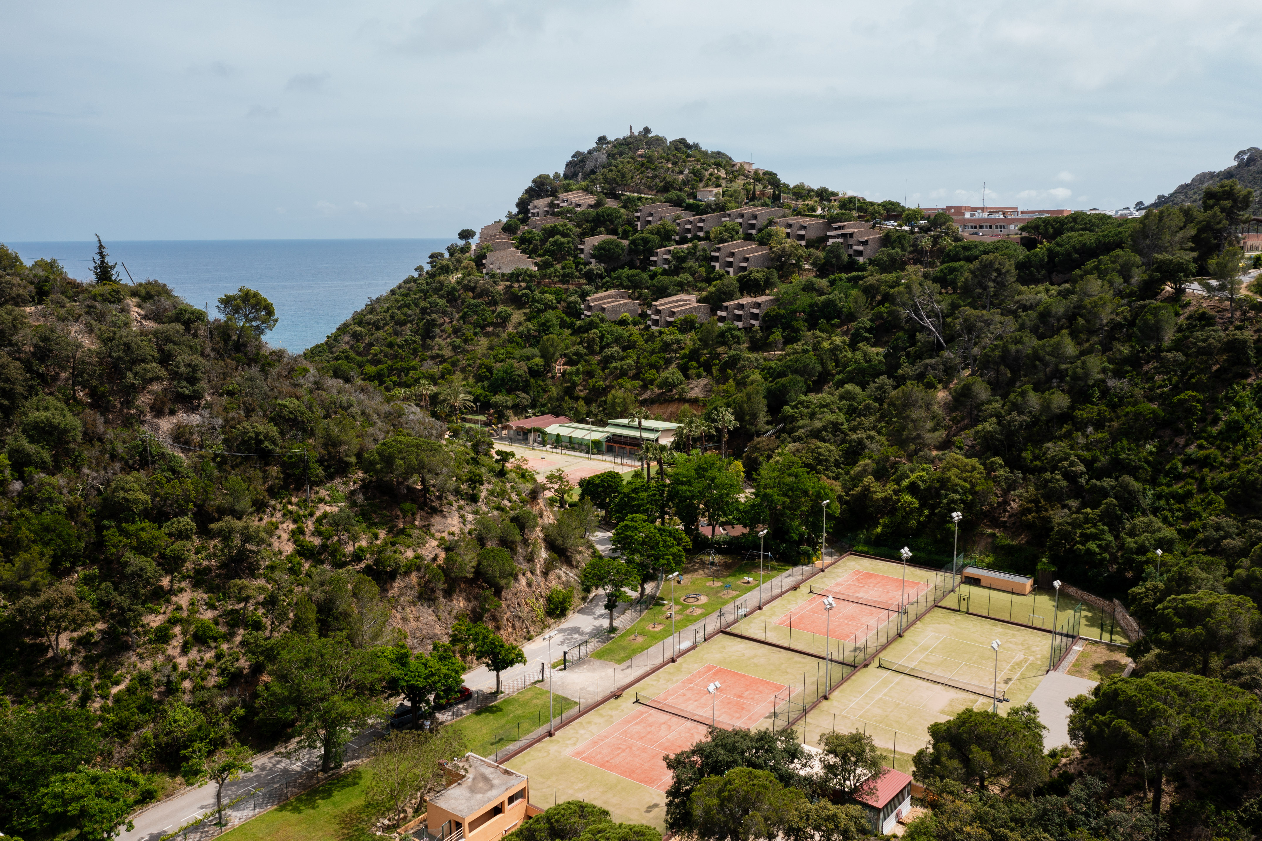 a tennis court and a large hill with trees and buildings