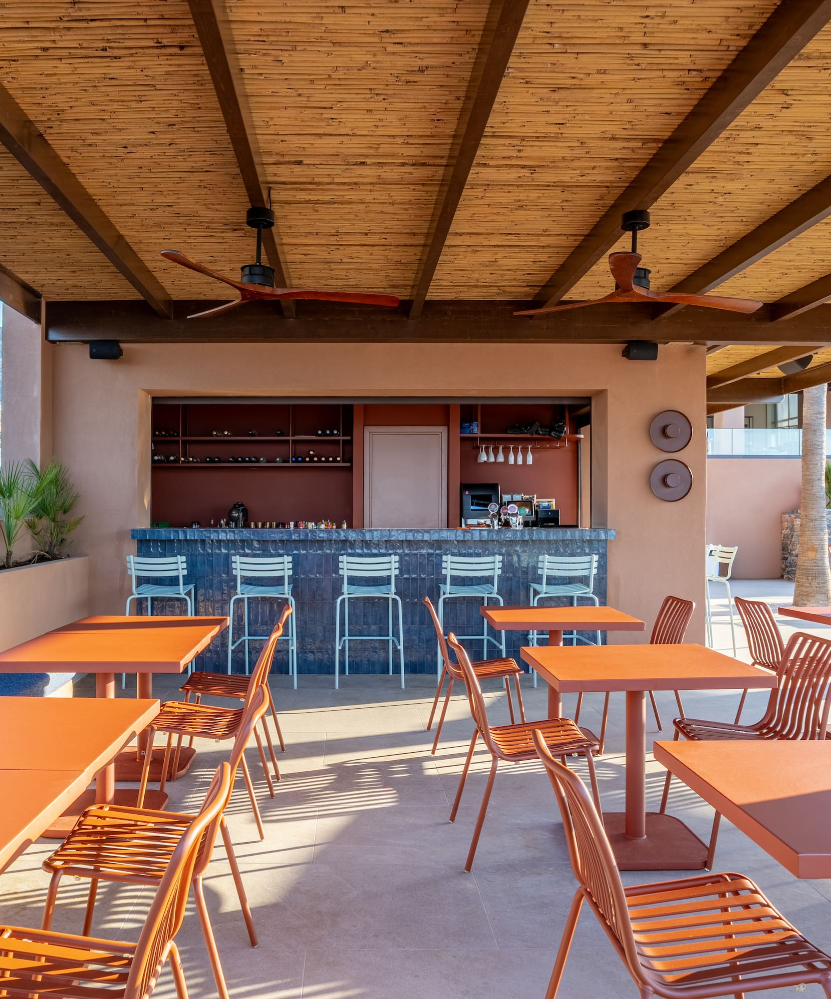 Outdoor resort bar with orange tables, bar stools, and bamboo ceiling.