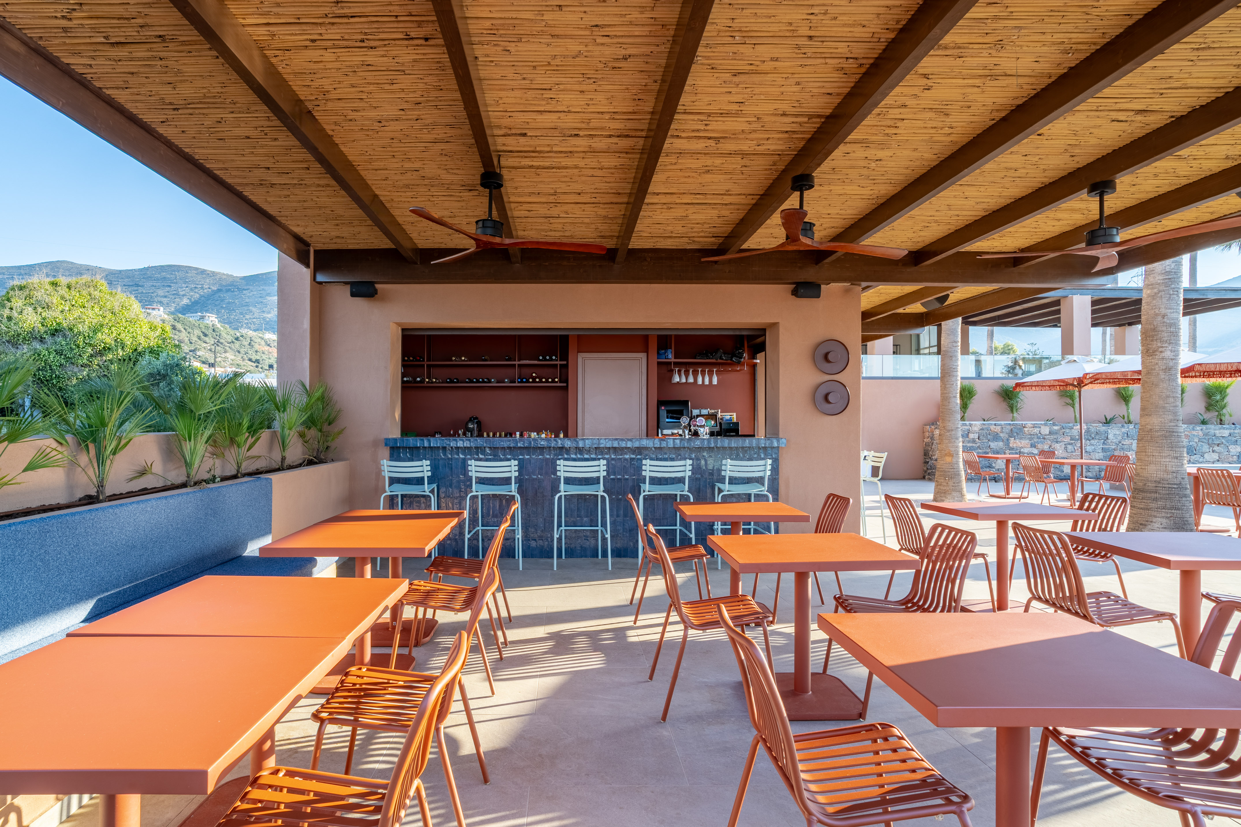 Outdoor resort bar with orange tables, bar stools, and bamboo ceiling.