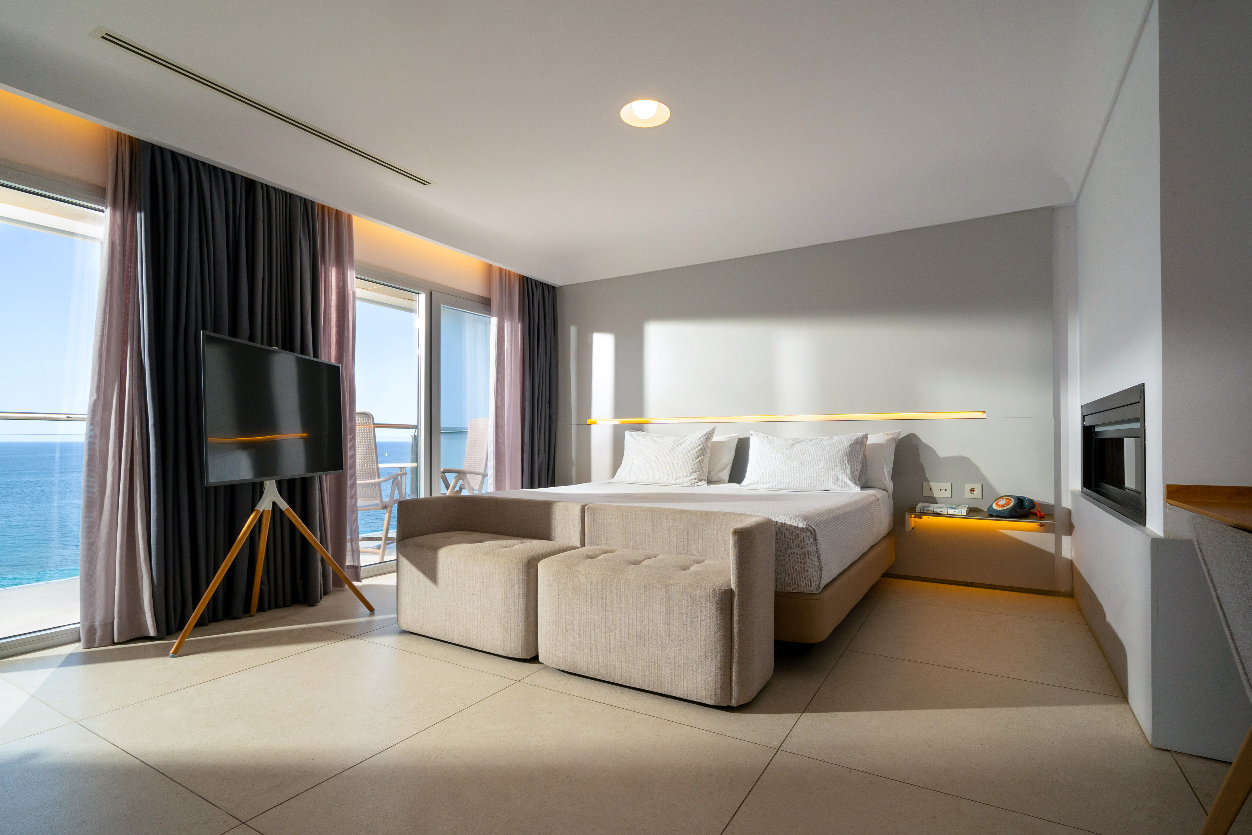 Modern hotel room with sea view, balcony, large bed, and TV.