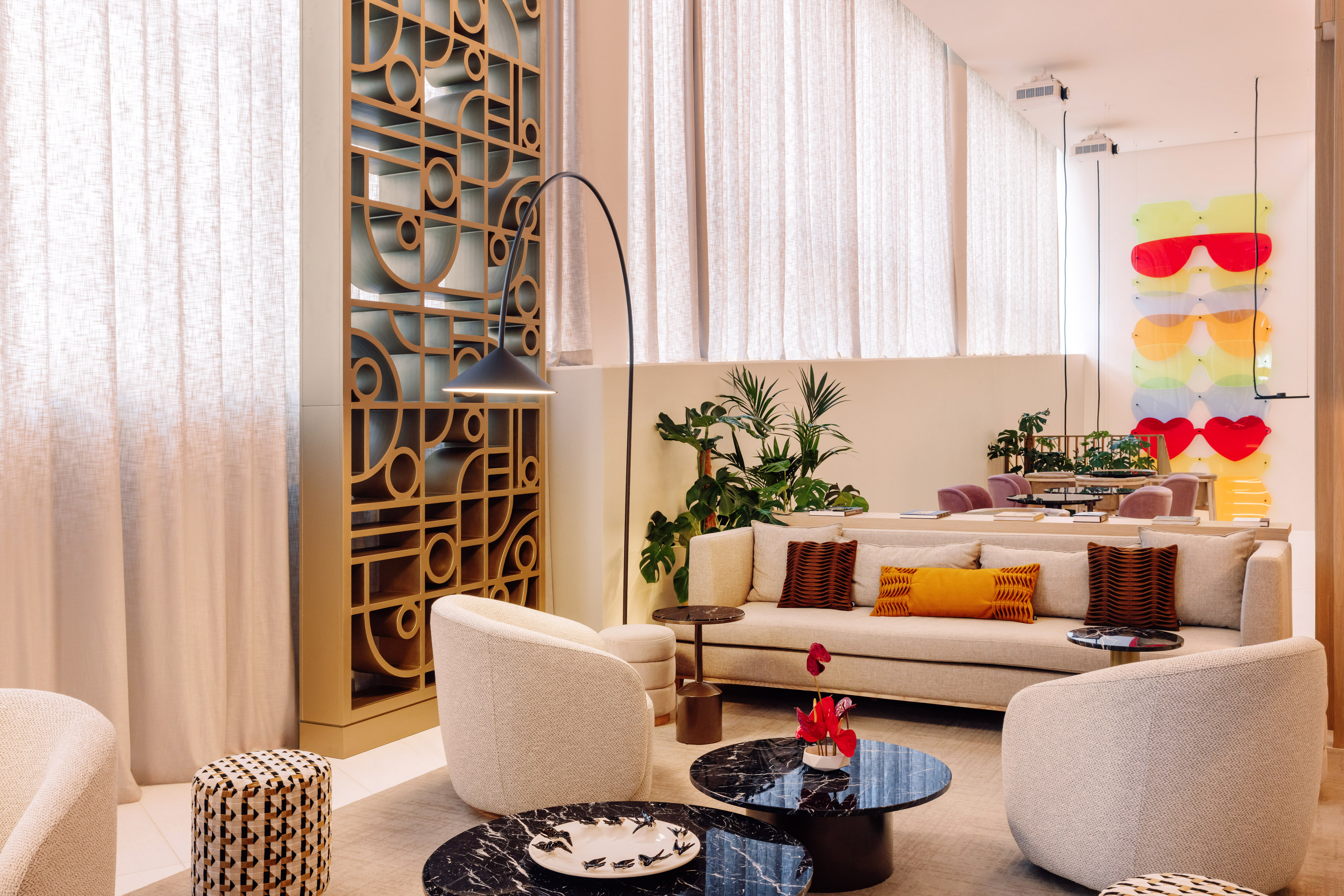 Modern lounge with neutral furniture, wooden screen, plants, and colorful art.
