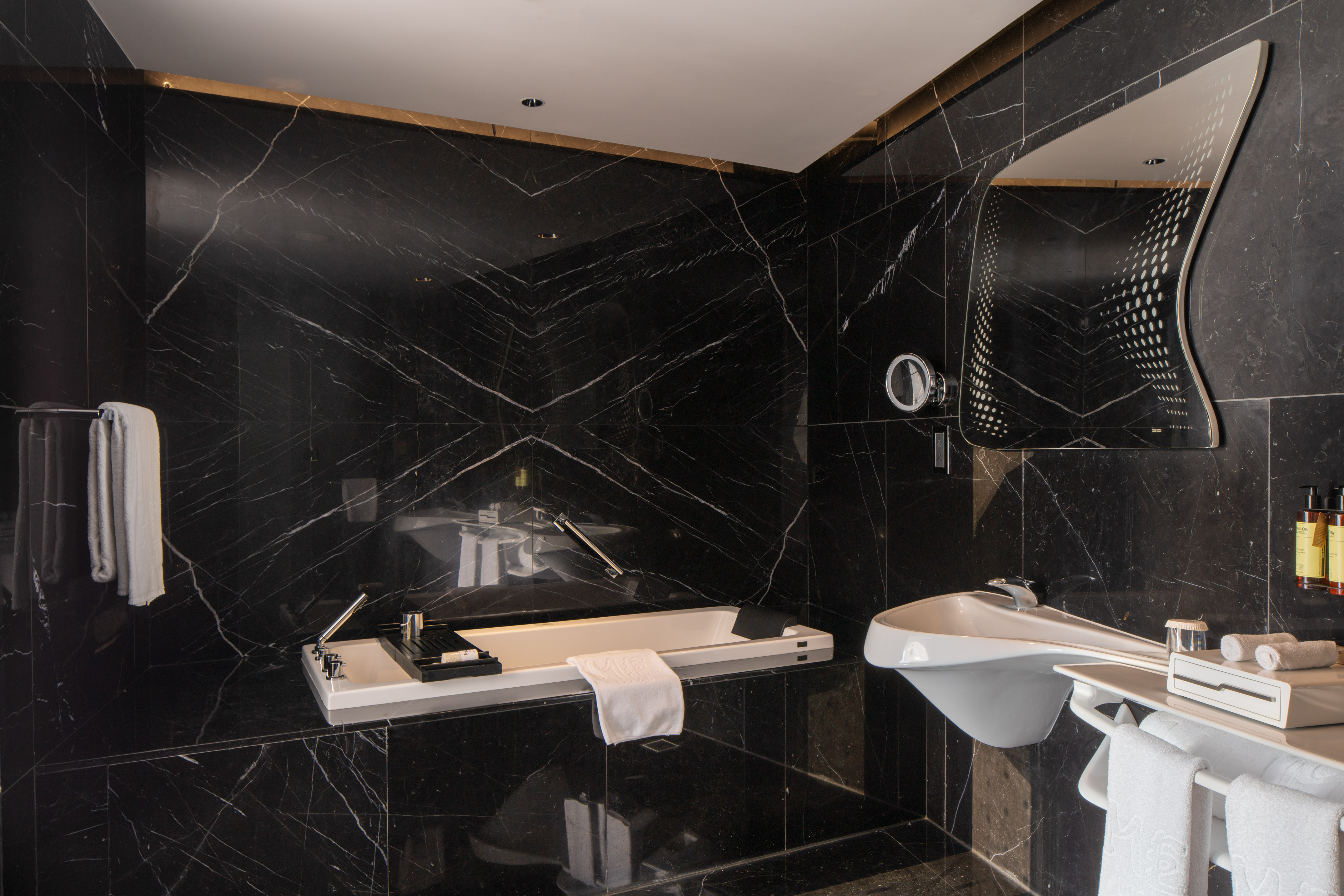 Elegant black marble bathroom with modern white tub, designer sink, and mirror.