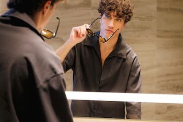 a man holding glasses in front of a mirror