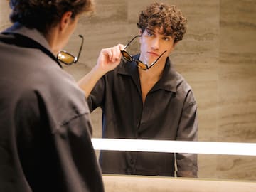 a man holding glasses in front of a mirror