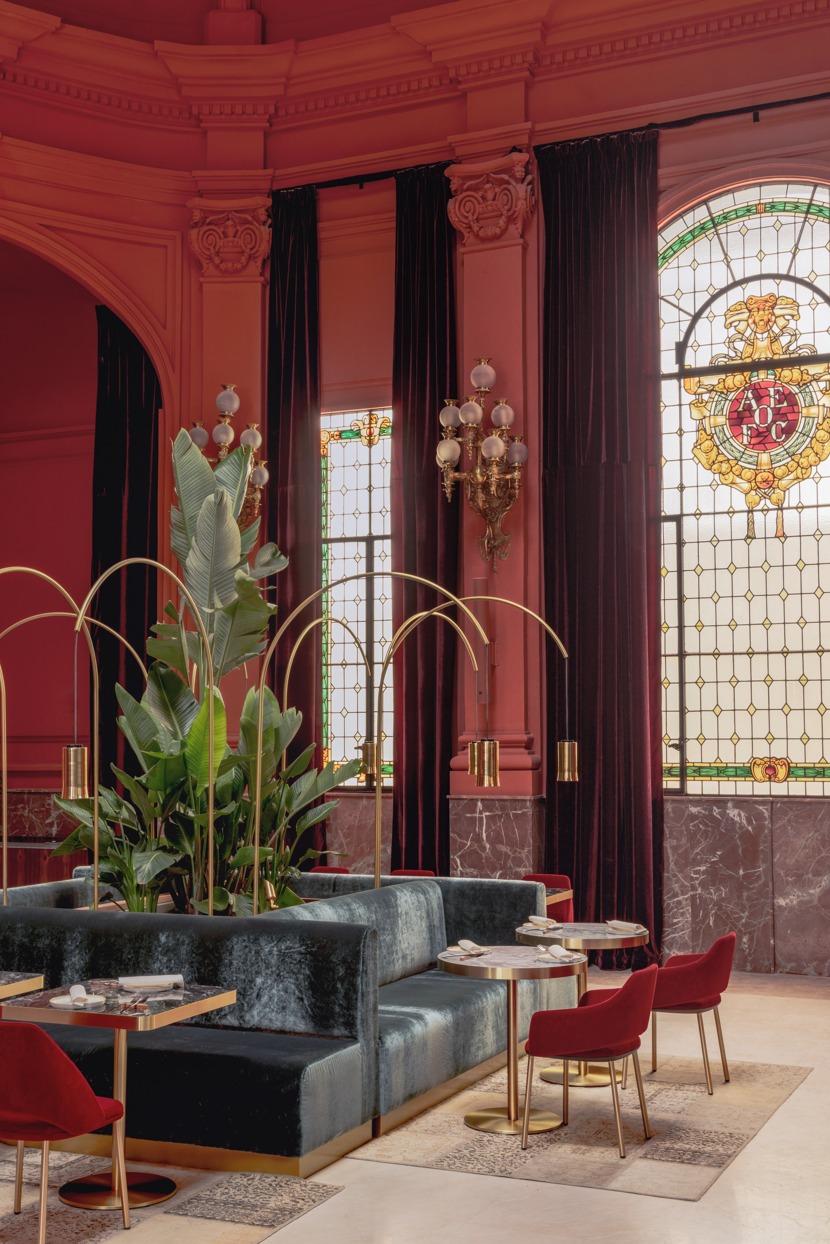 Red luxury restaurant interior with velvet seating, gold tables, and stained glass.