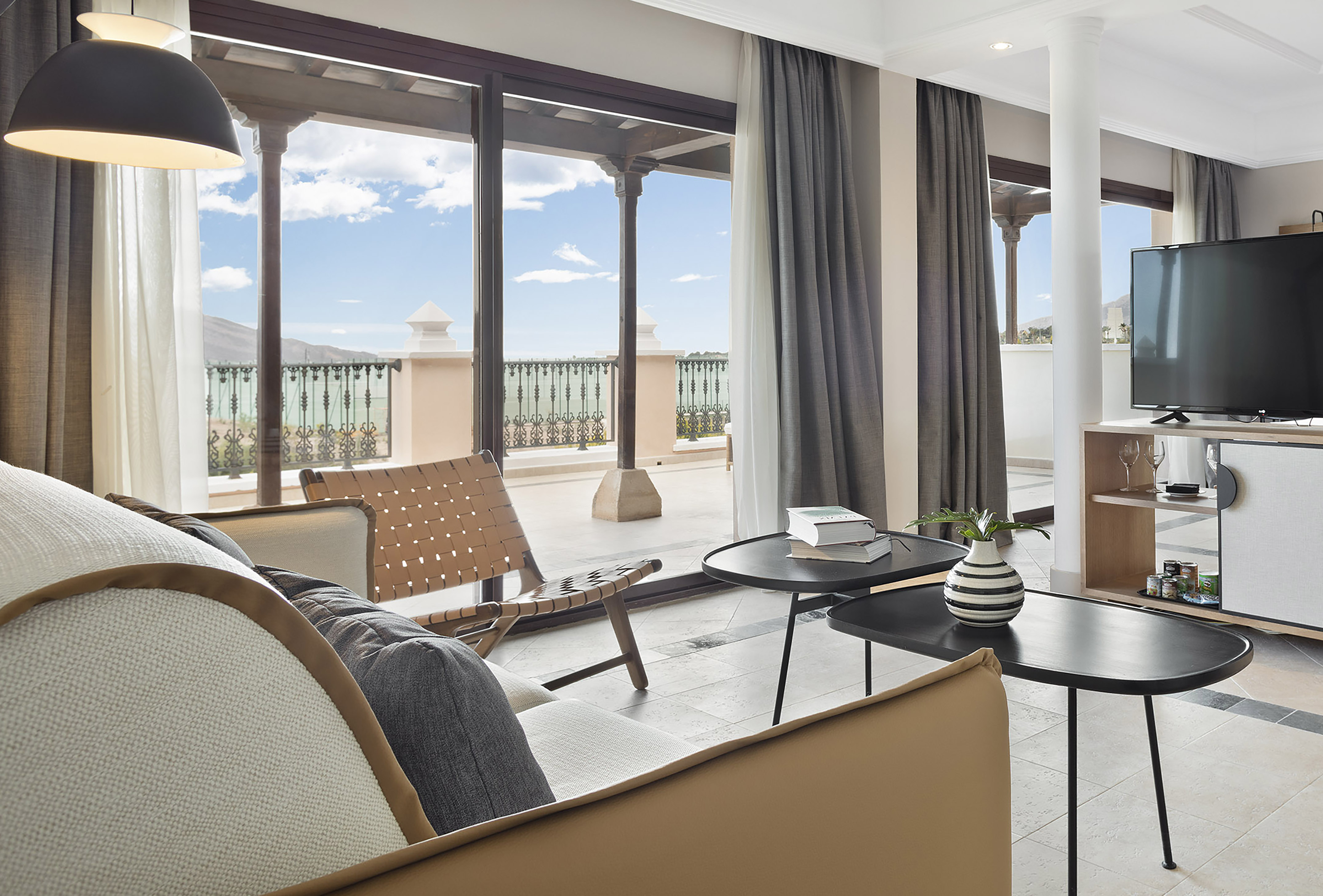 Modern hotel living room with balcony, sofa, and ocean mountain view.