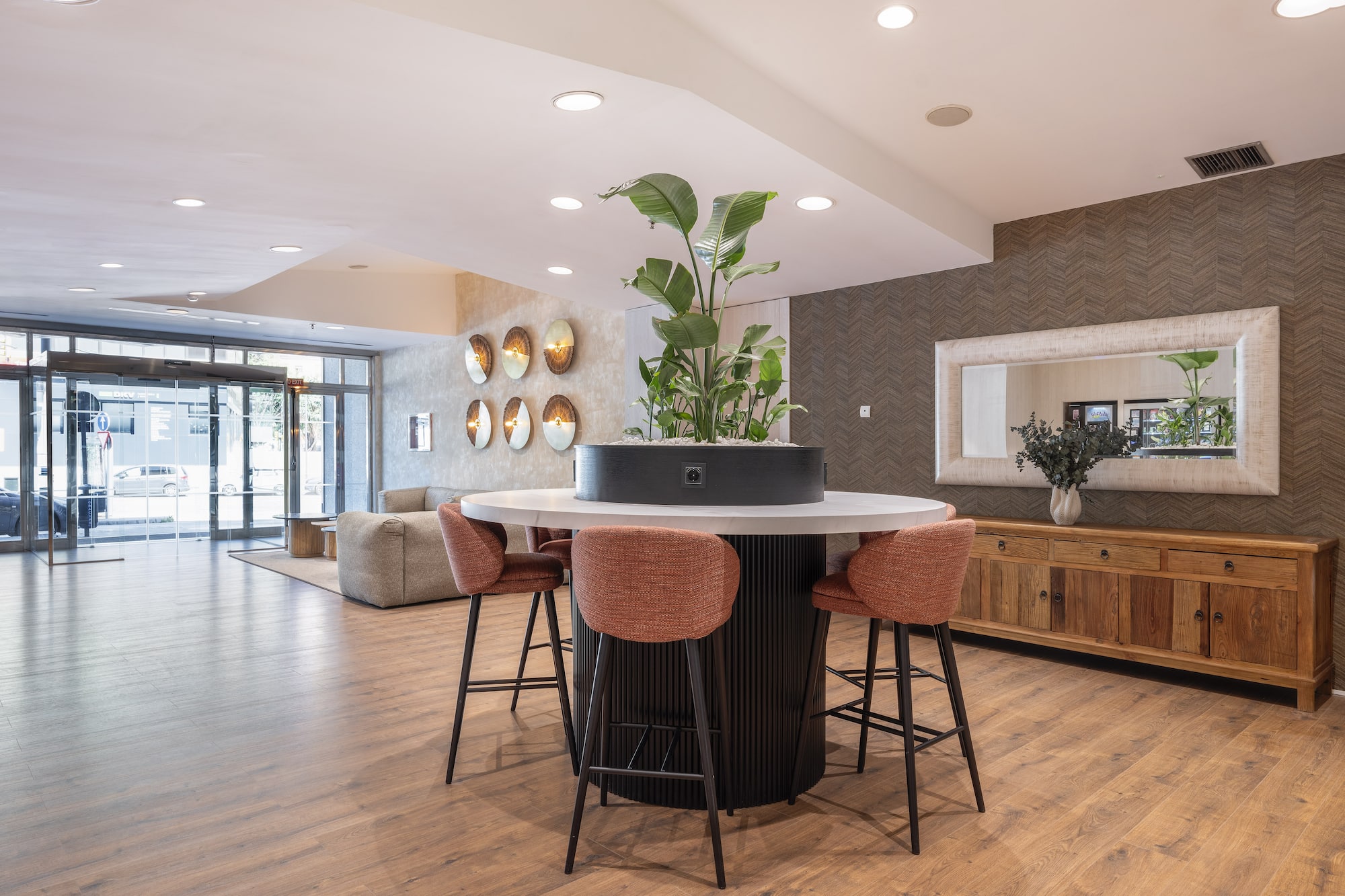 Modern hotel lobby with circular plant table, bar stools, and wood floor.