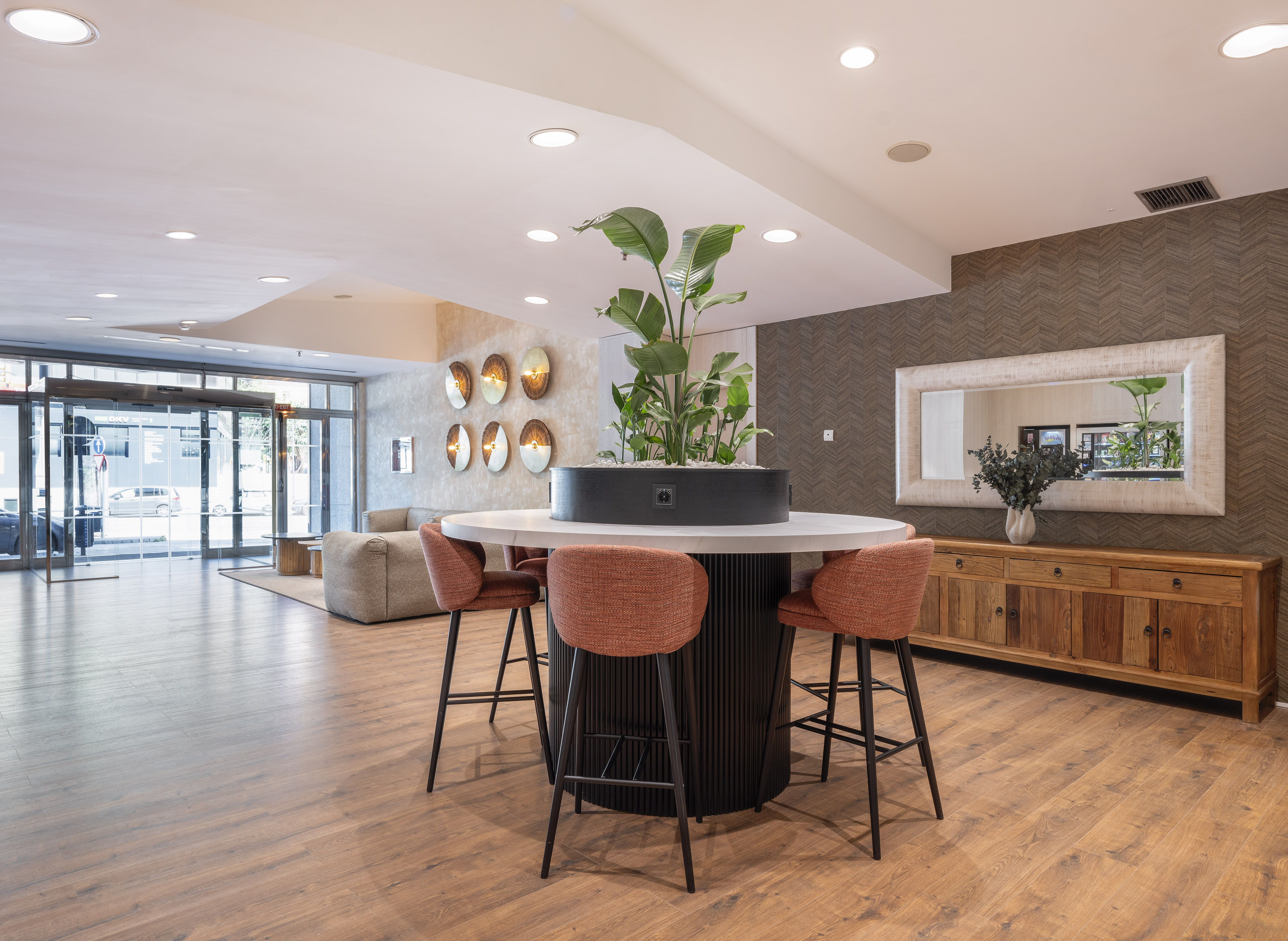 Modern hotel lobby with circular plant table, bar stools, and wood floor.
