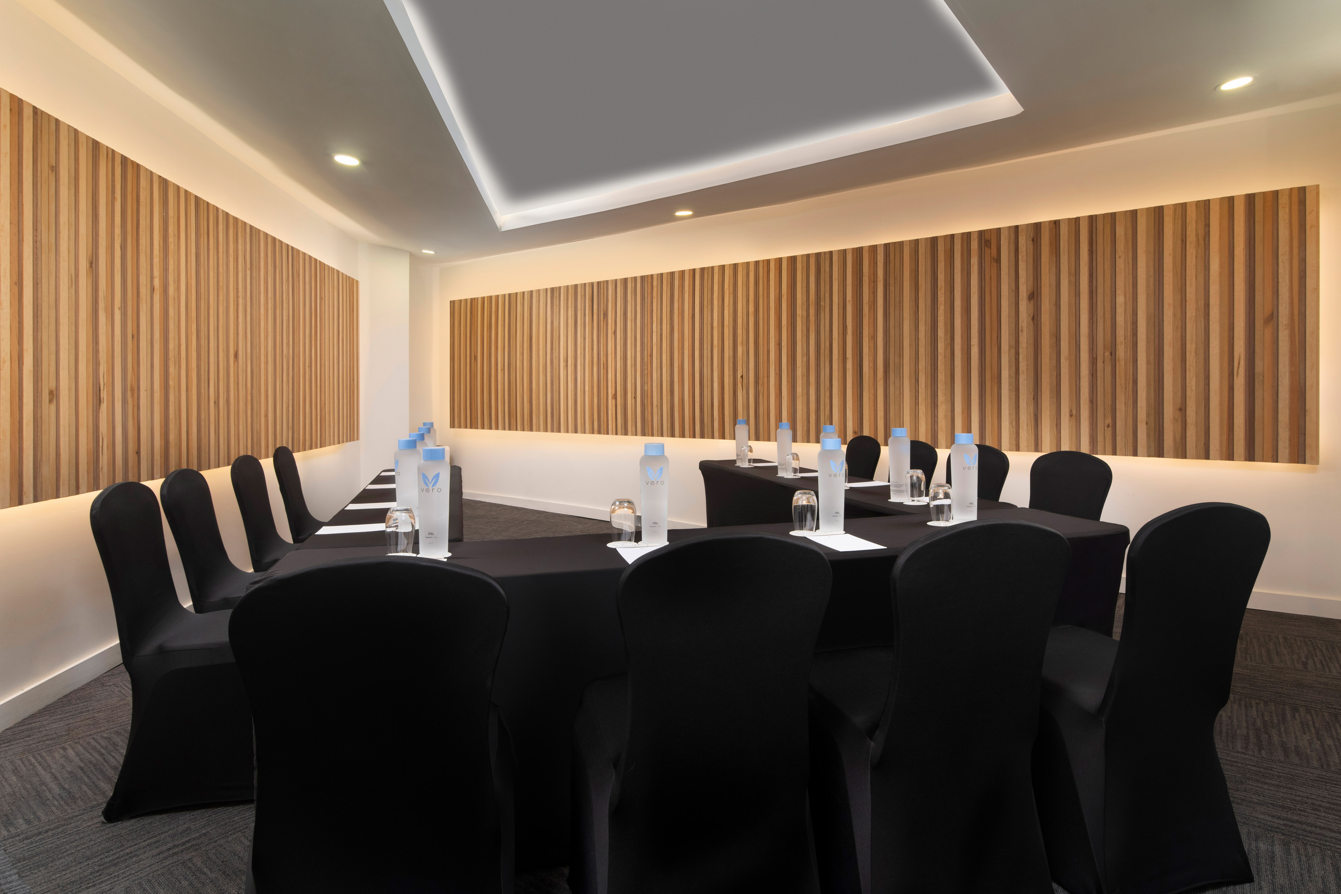 Modern conference room with U-shaped table, black chairs, wood paneling, and ambient lighting.