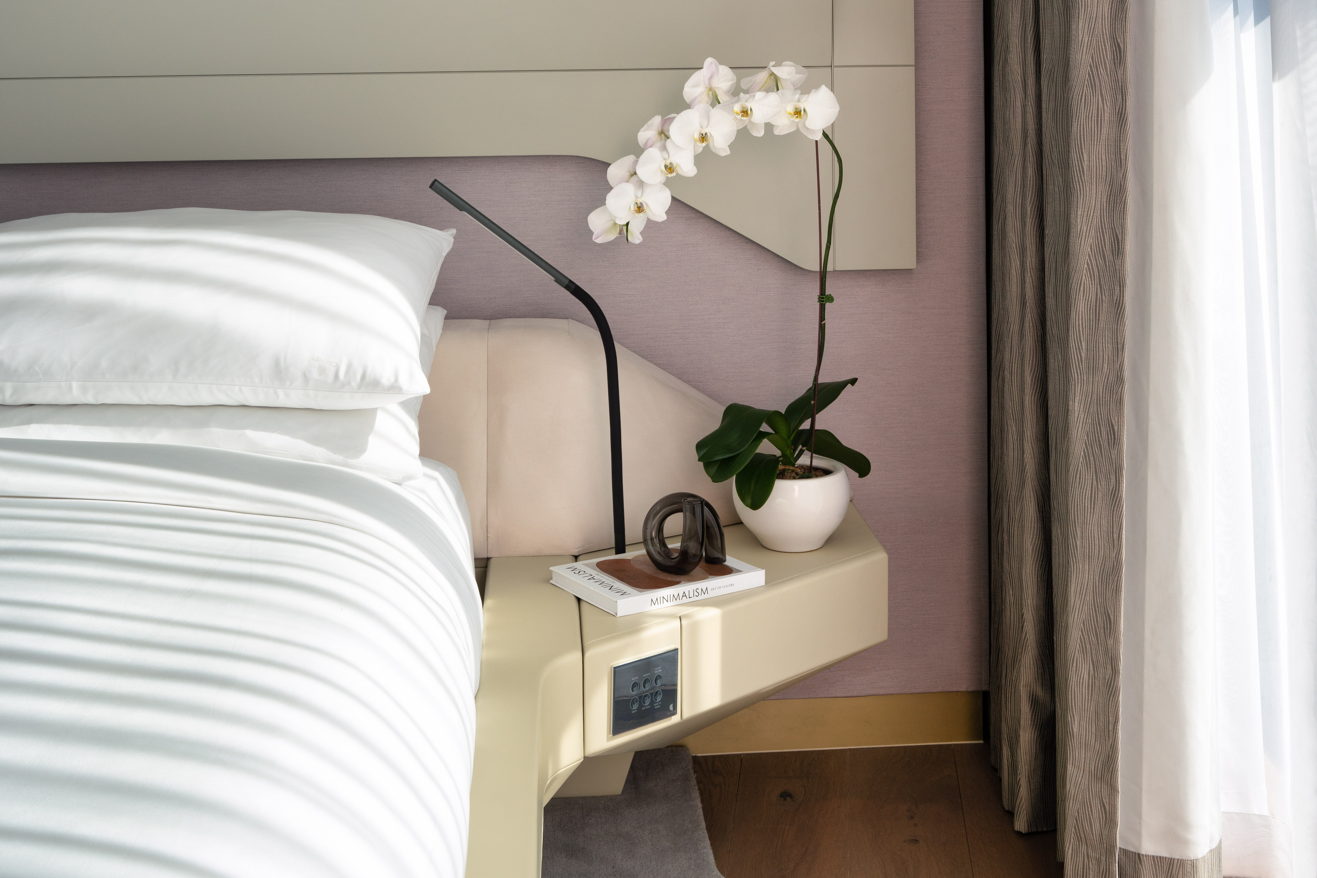 Modern bedroom with white bed, orchid, integrated nightstand, and reading lamp.