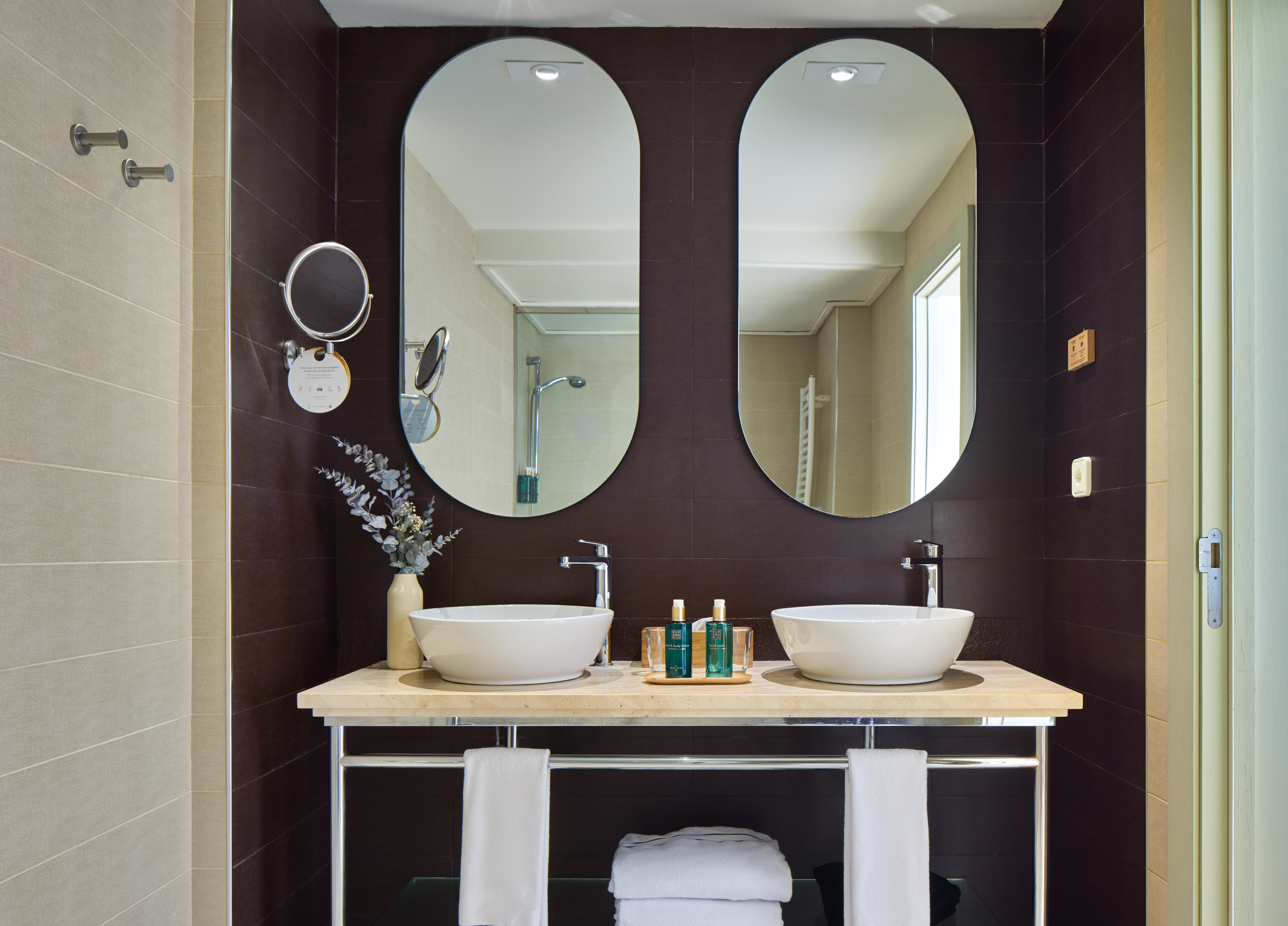 Modern hotel bathroom with double vessel sinks, oval mirrors, and fresh towels.