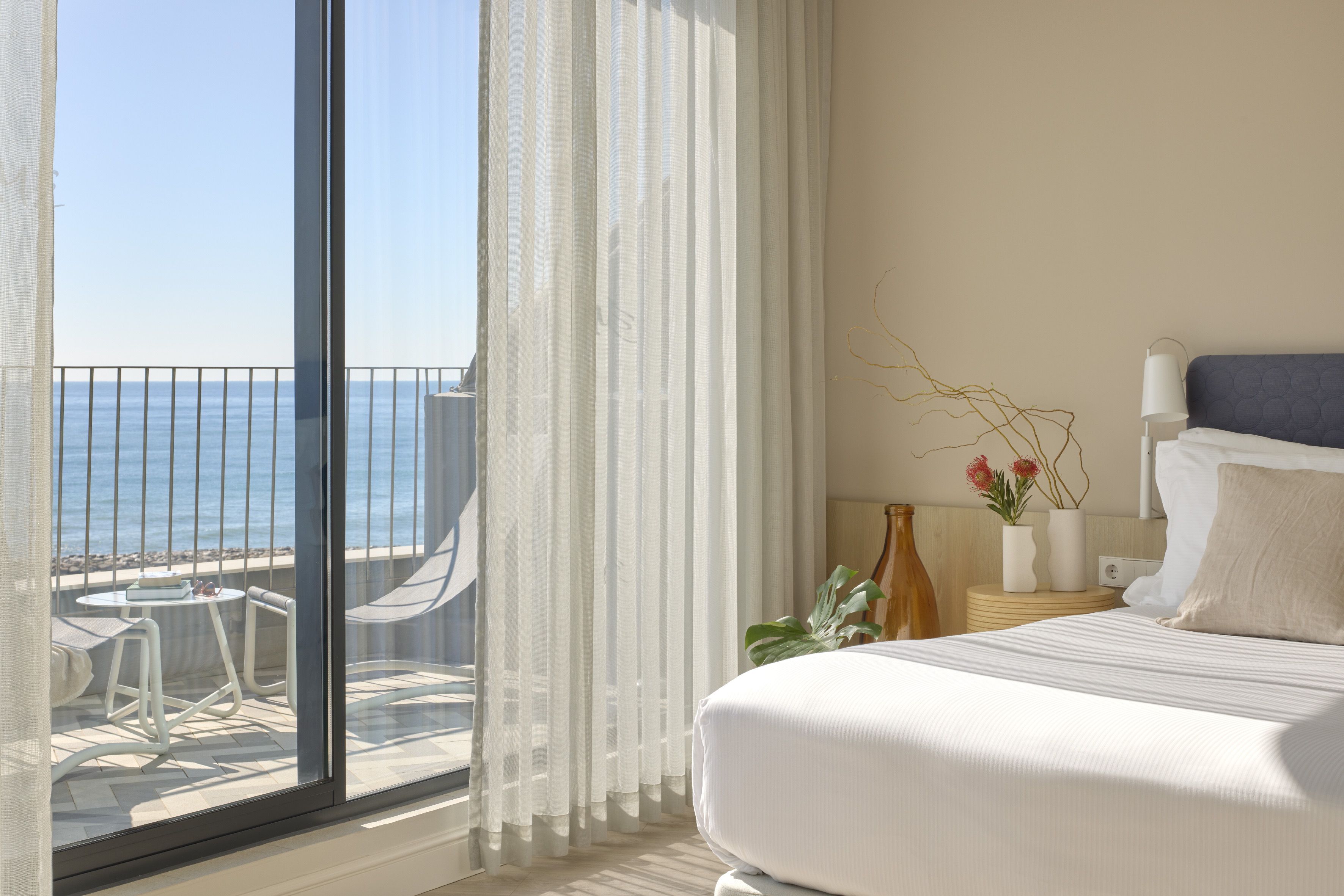 Hotel room with sea view balcony, white bed, and modern coastal decor.