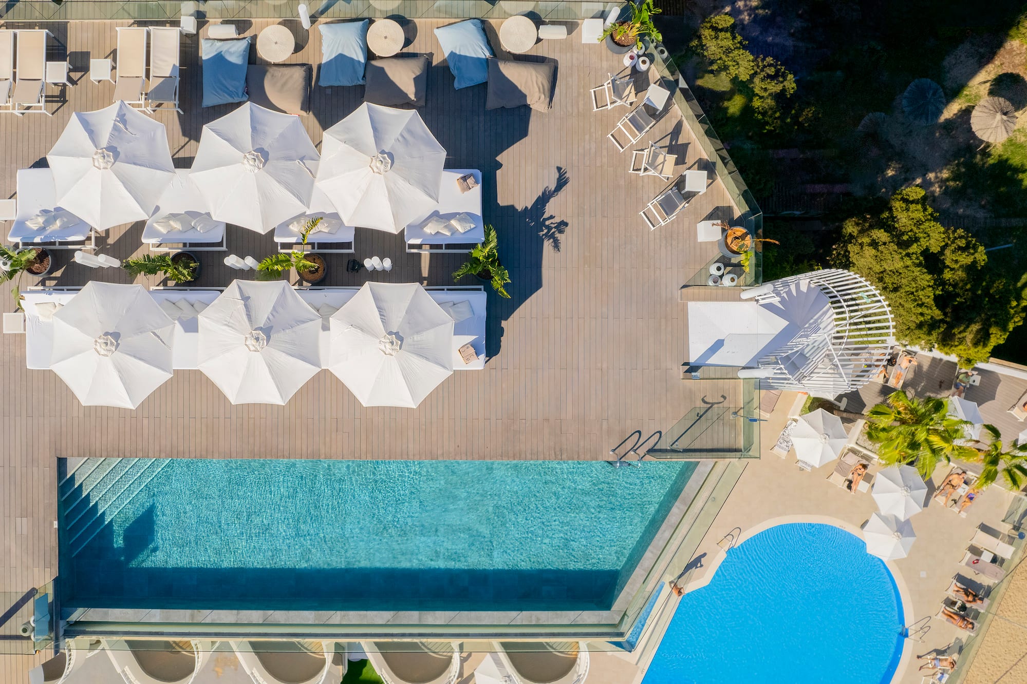 Luxury resort pool deck with sunbeds, white umbrellas, blue pools.