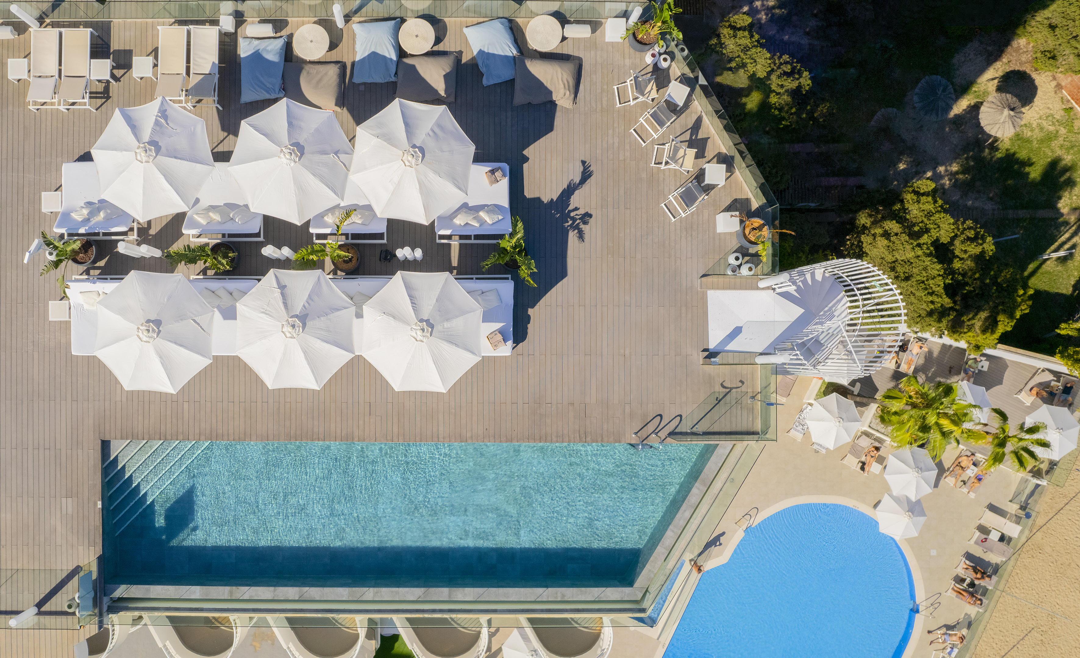 Luxury resort pool deck with sunbeds, white umbrellas, blue pools.