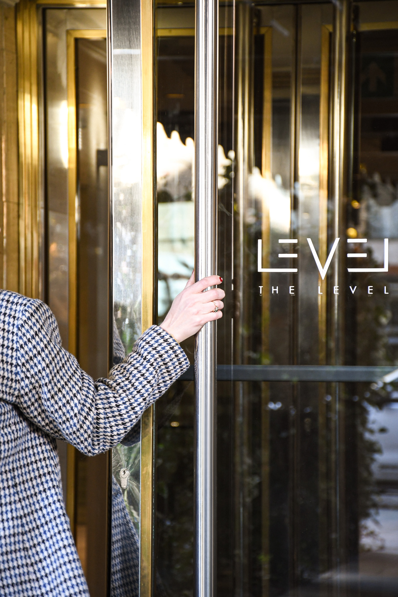 Hand in houndstooth jacket opening glass entrance door to The Level.