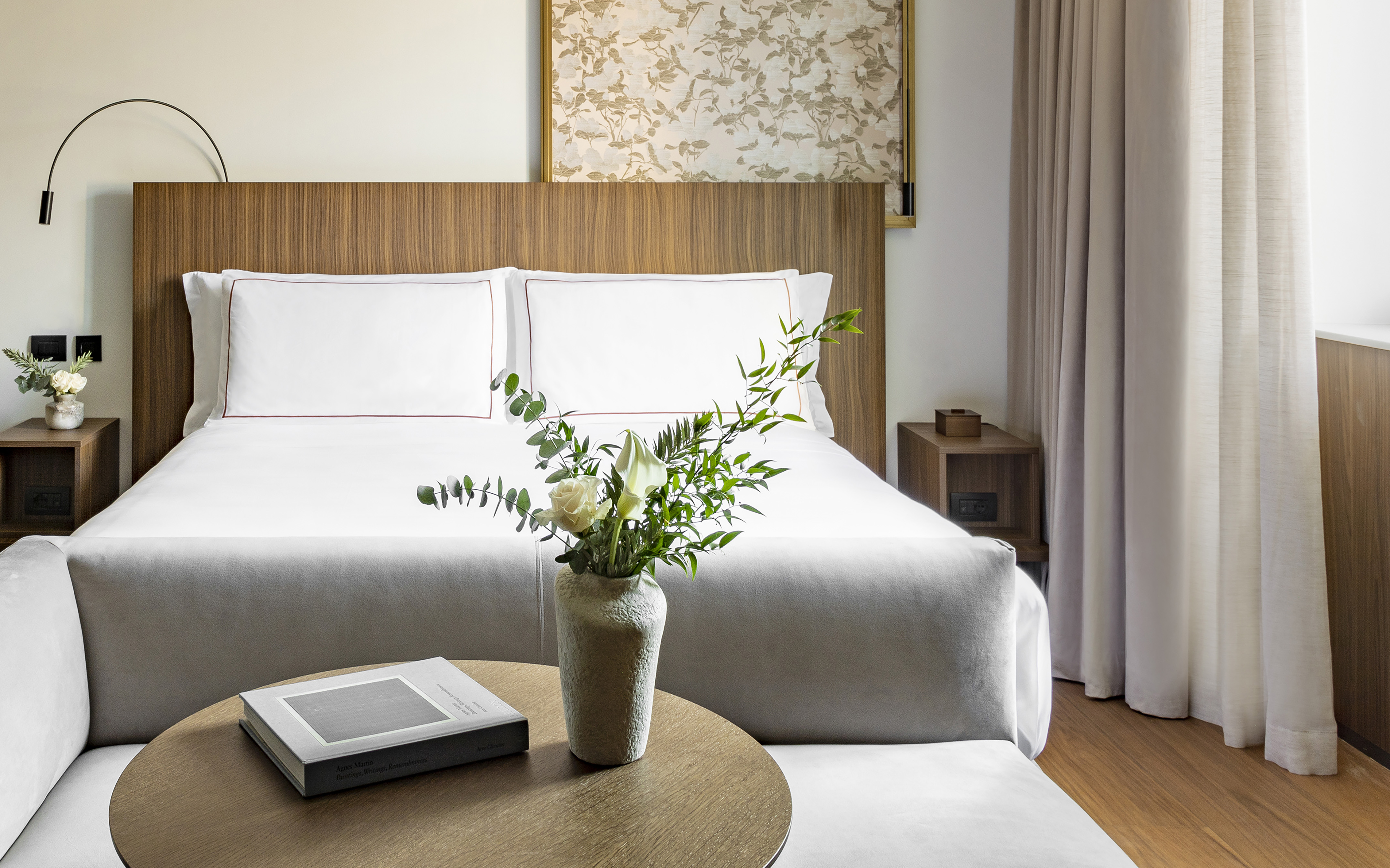 Elegant hotel room with white bed, wooden headboard, and floral decor.