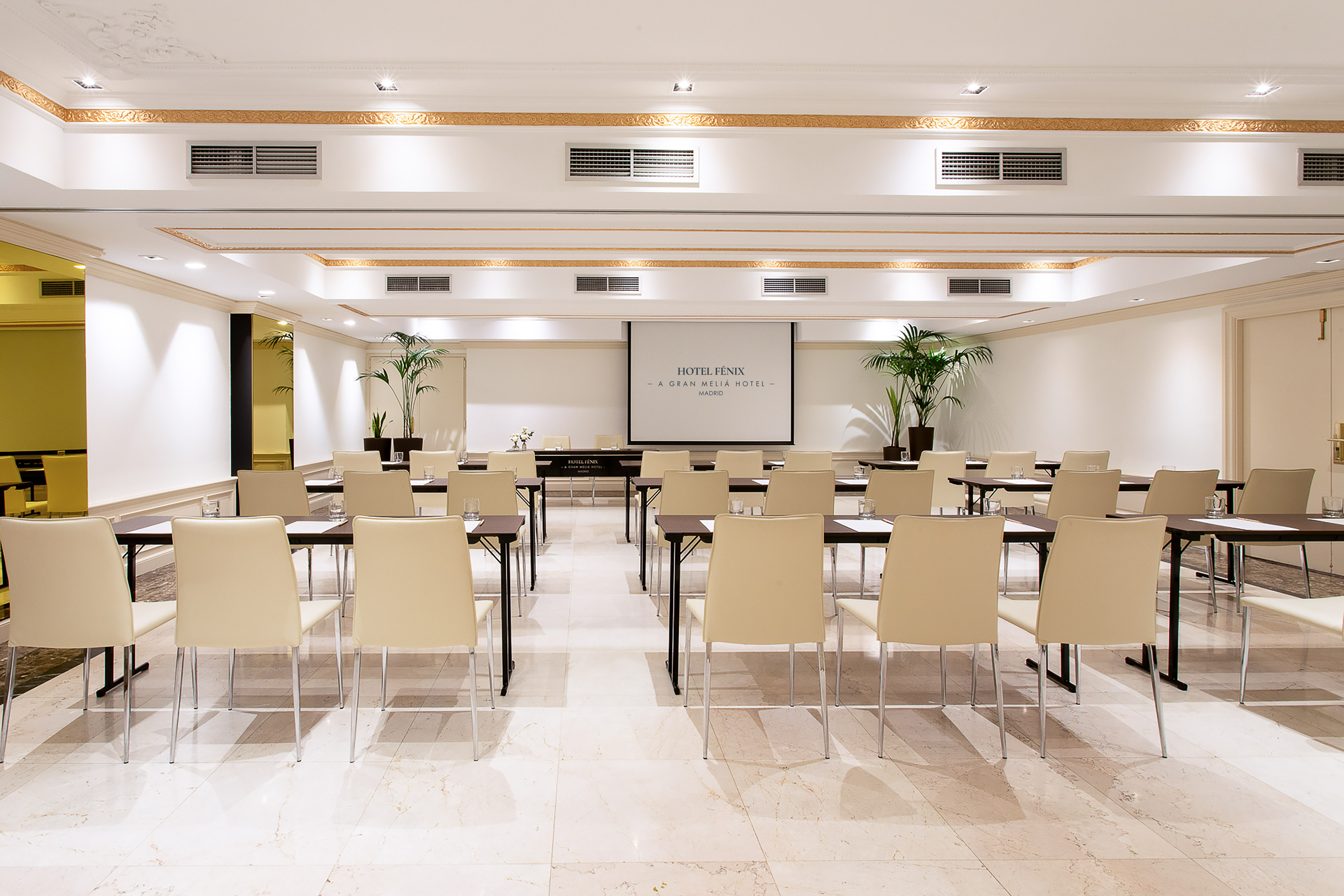 Elegant Hotel Fénix Madrid conference room with screen, tables, and chairs.