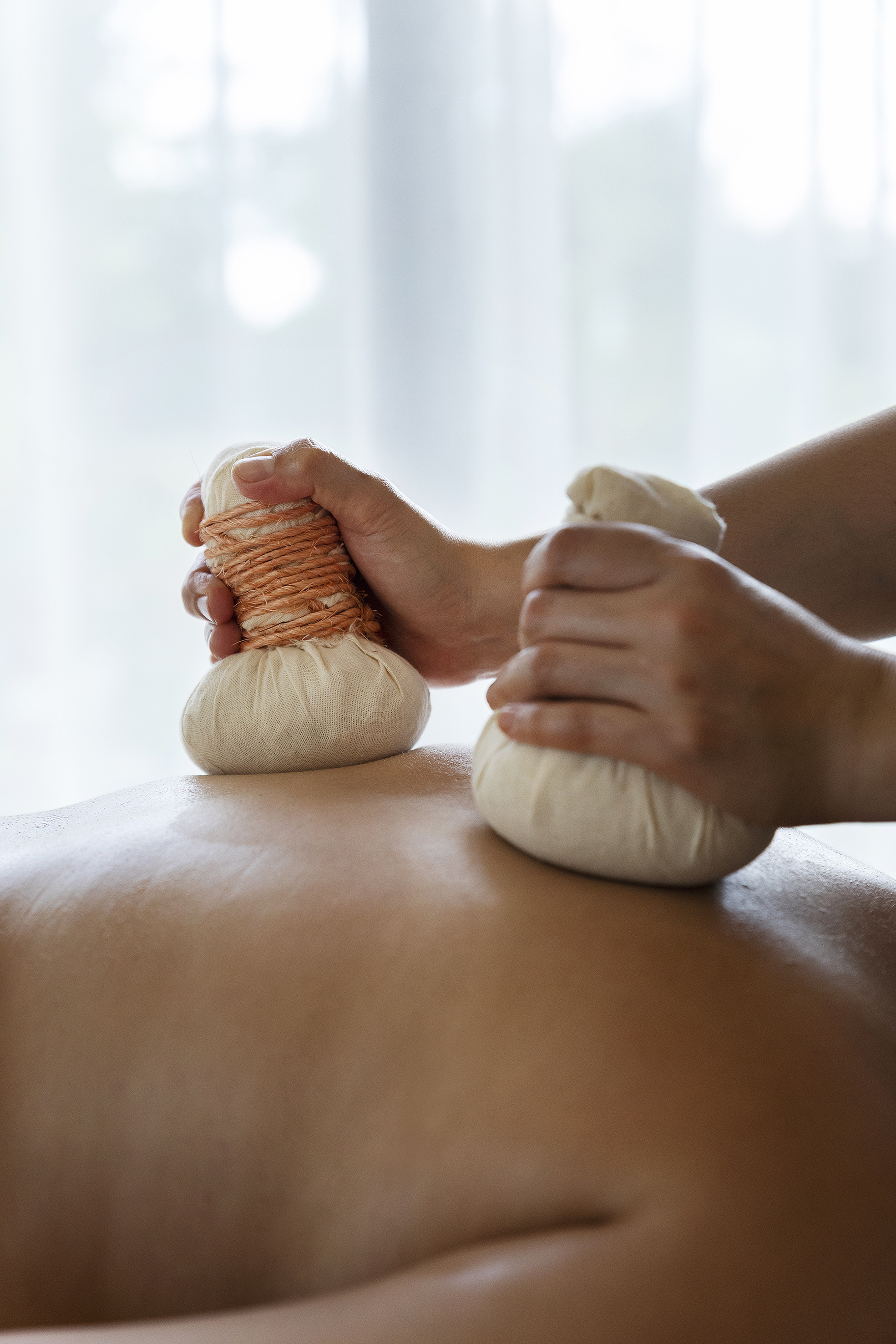 Hands applying herbal compress balls to a person's back for spa massage.