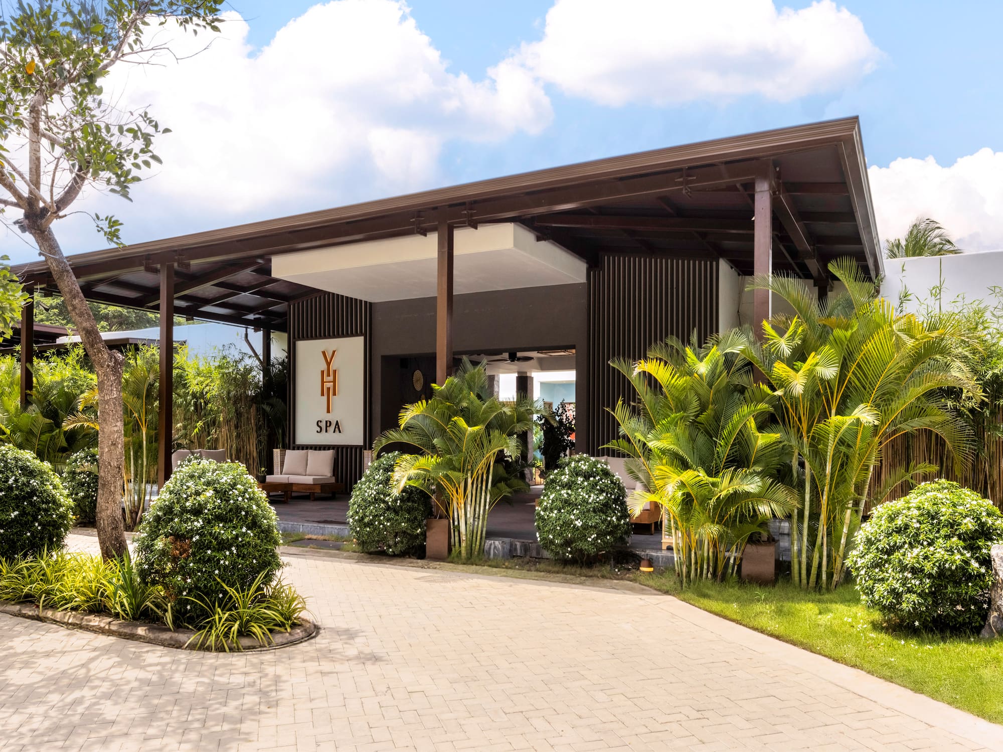 Tropical YHI SPA entrance, modern building with lush landscaping and paved drive.