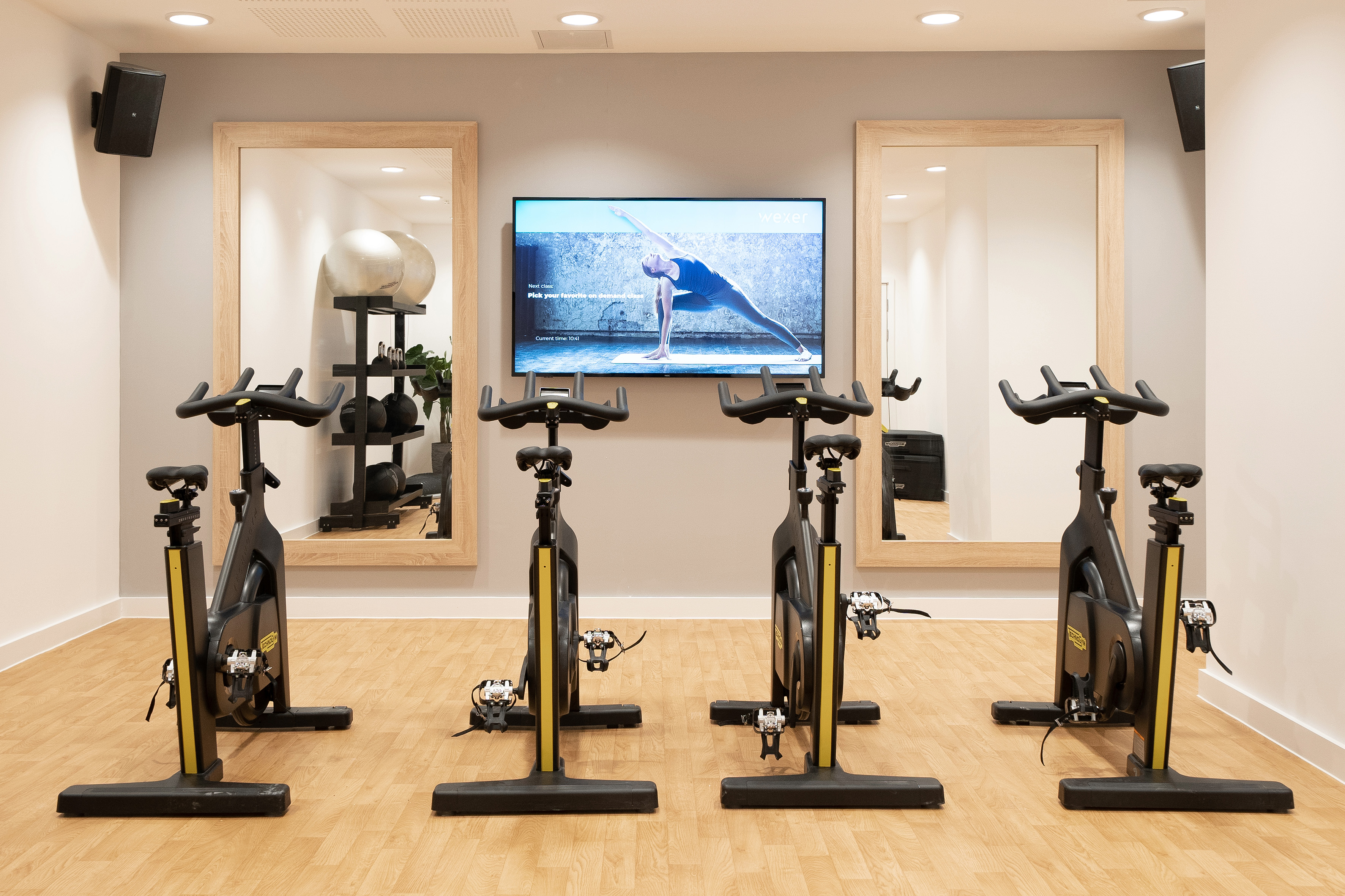 Four black and yellow spin bikes in a fitness studio with a virtual yoga screen.